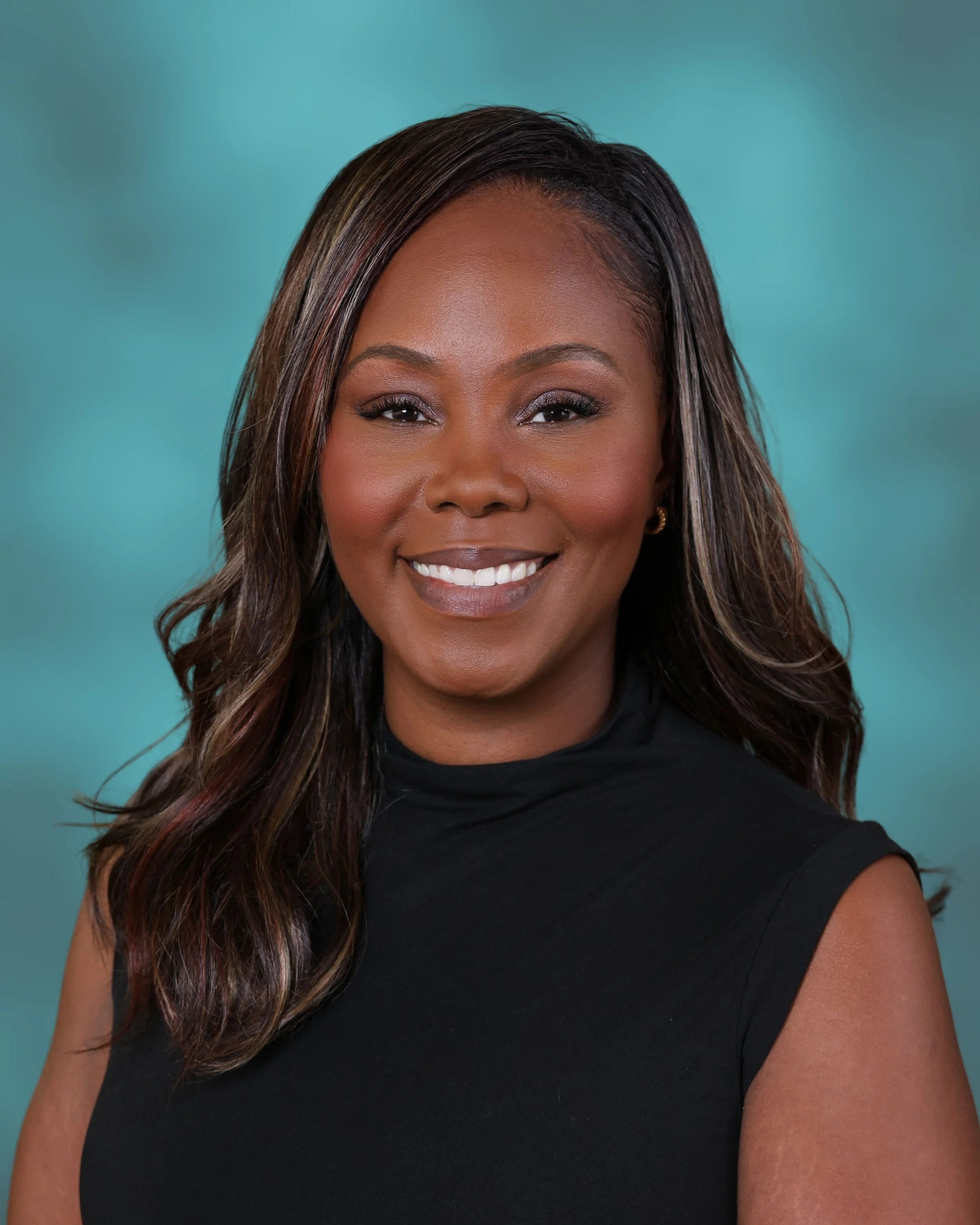Close-up of a woman smiling, with dark wavy hair, wearing a black sleeveless top, against a teal background.
