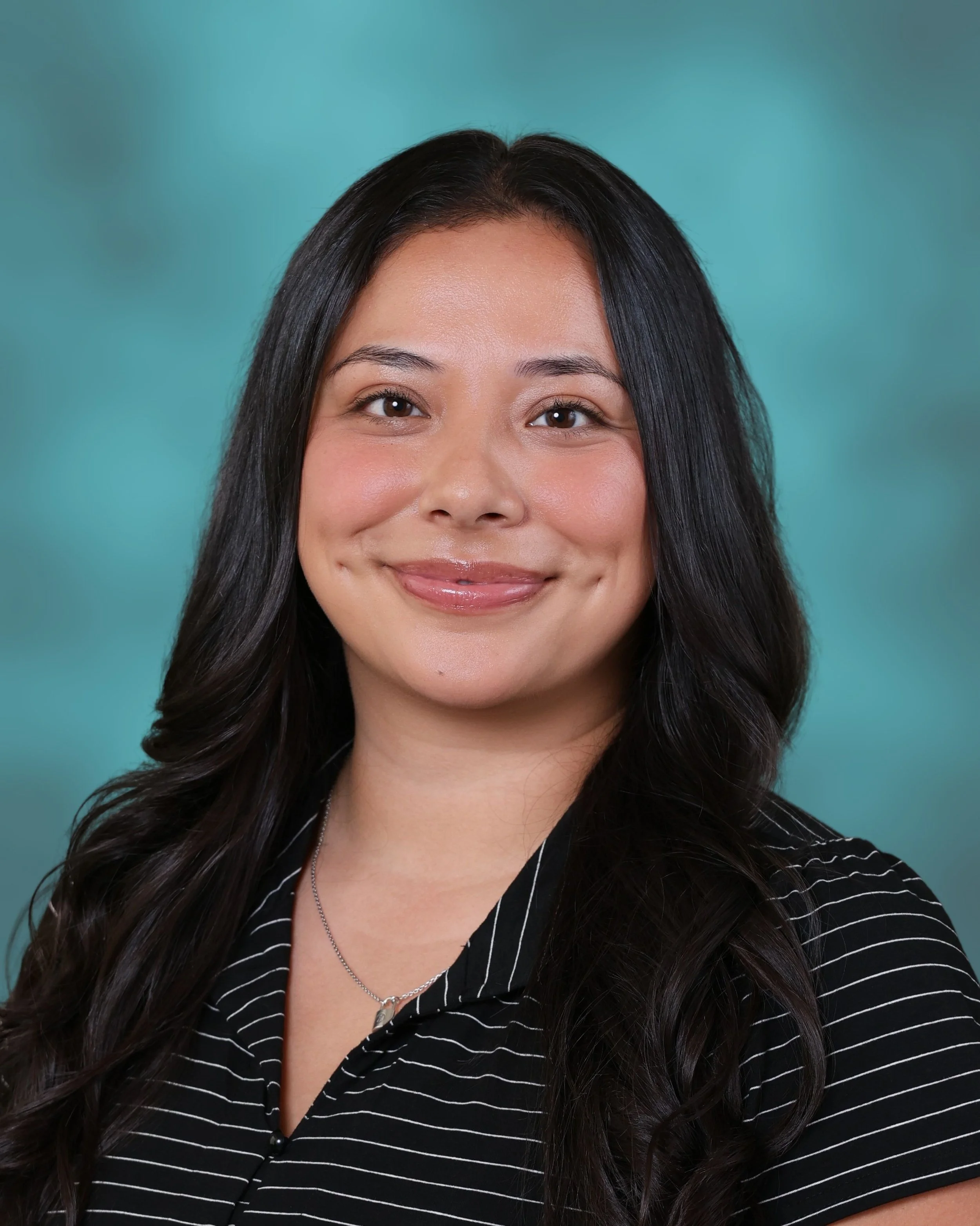A young woman with long dark hair smiling, wearing a black top with white pinstripes and a necklace, against a turquoise background.