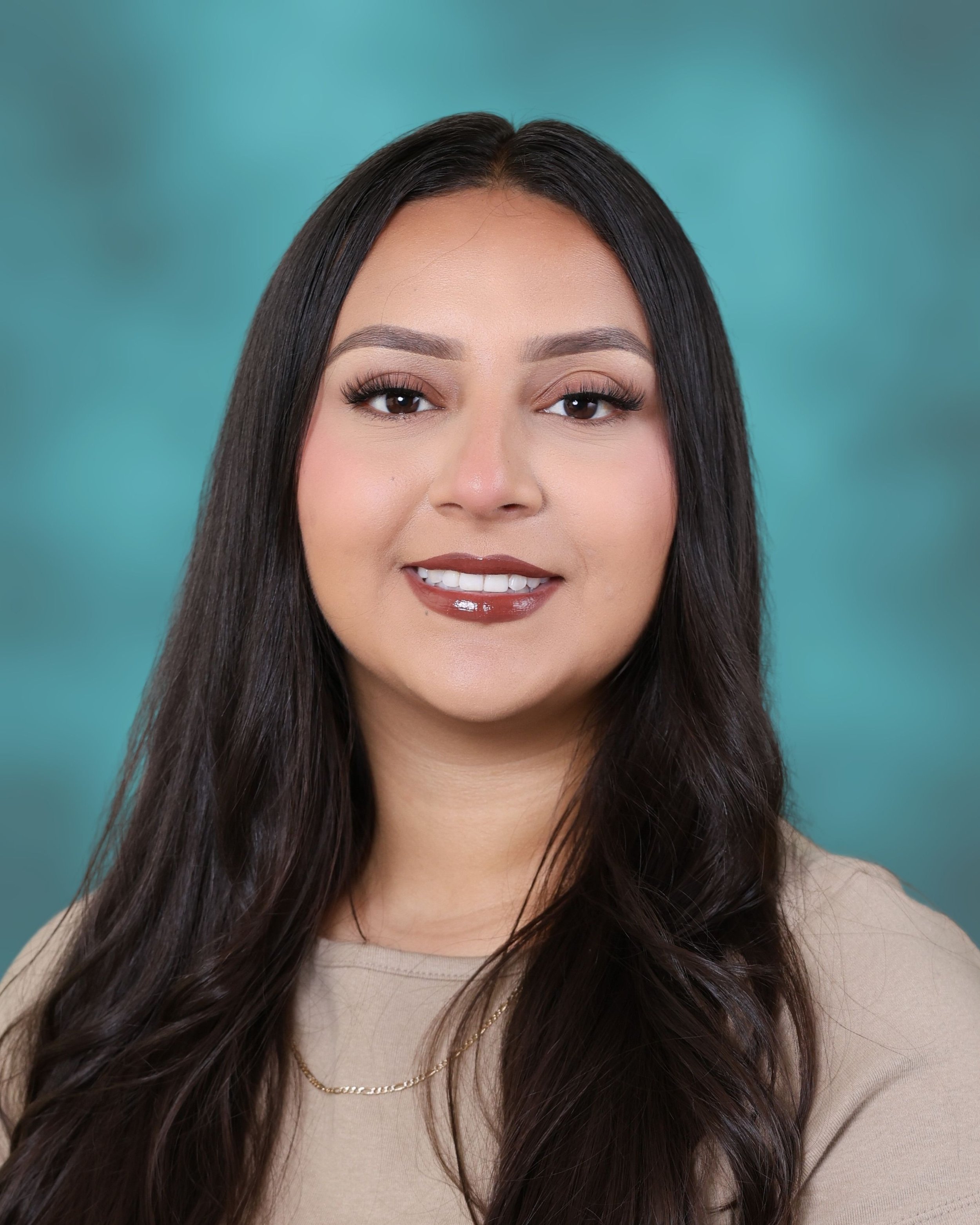 Close-up of a woman with long dark hair, wearing makeup and a beige top, smiling softly against a teal background.