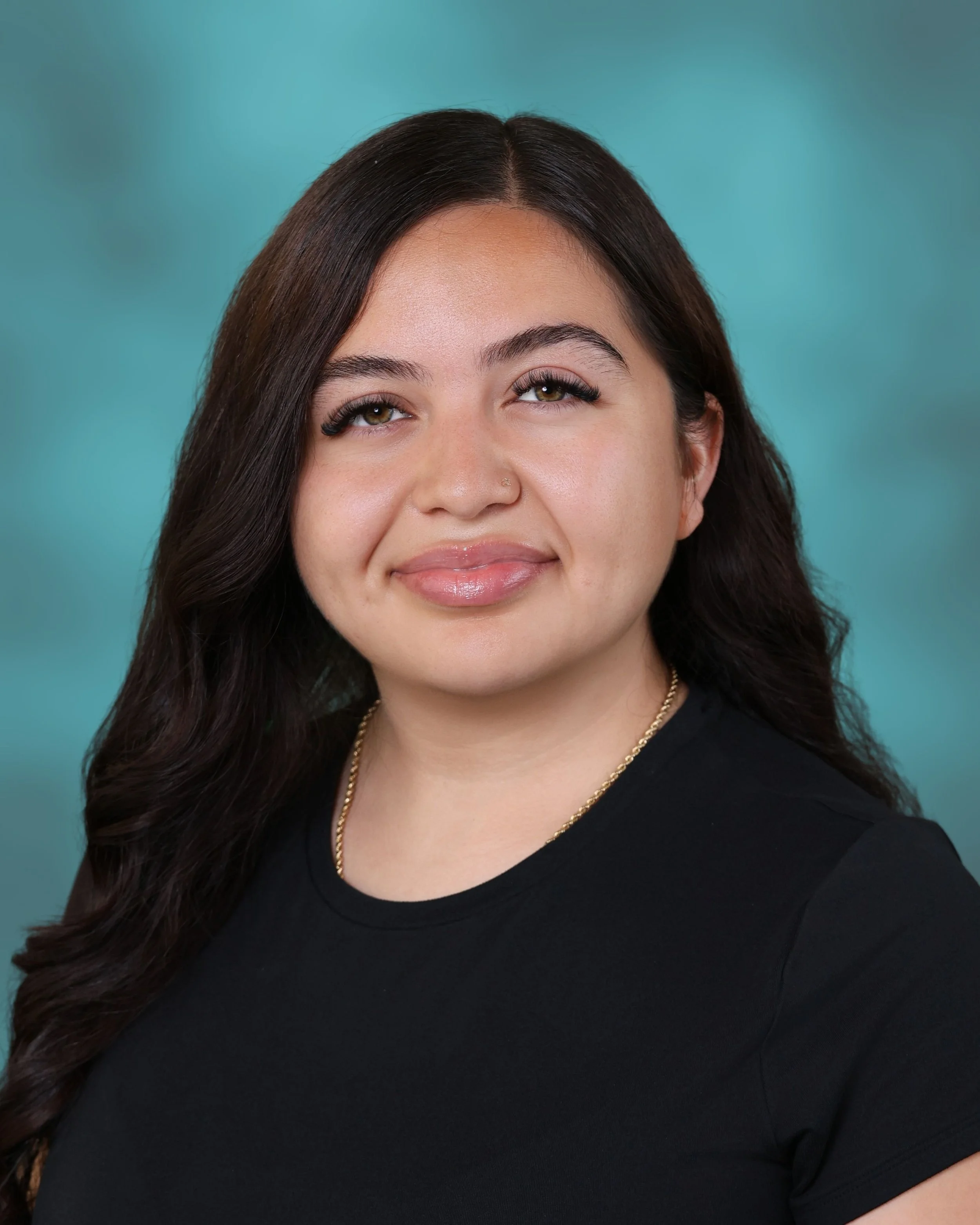 Close-up of a smiling woman with long dark hair, wearing a black top and gold necklace, against a teal background.