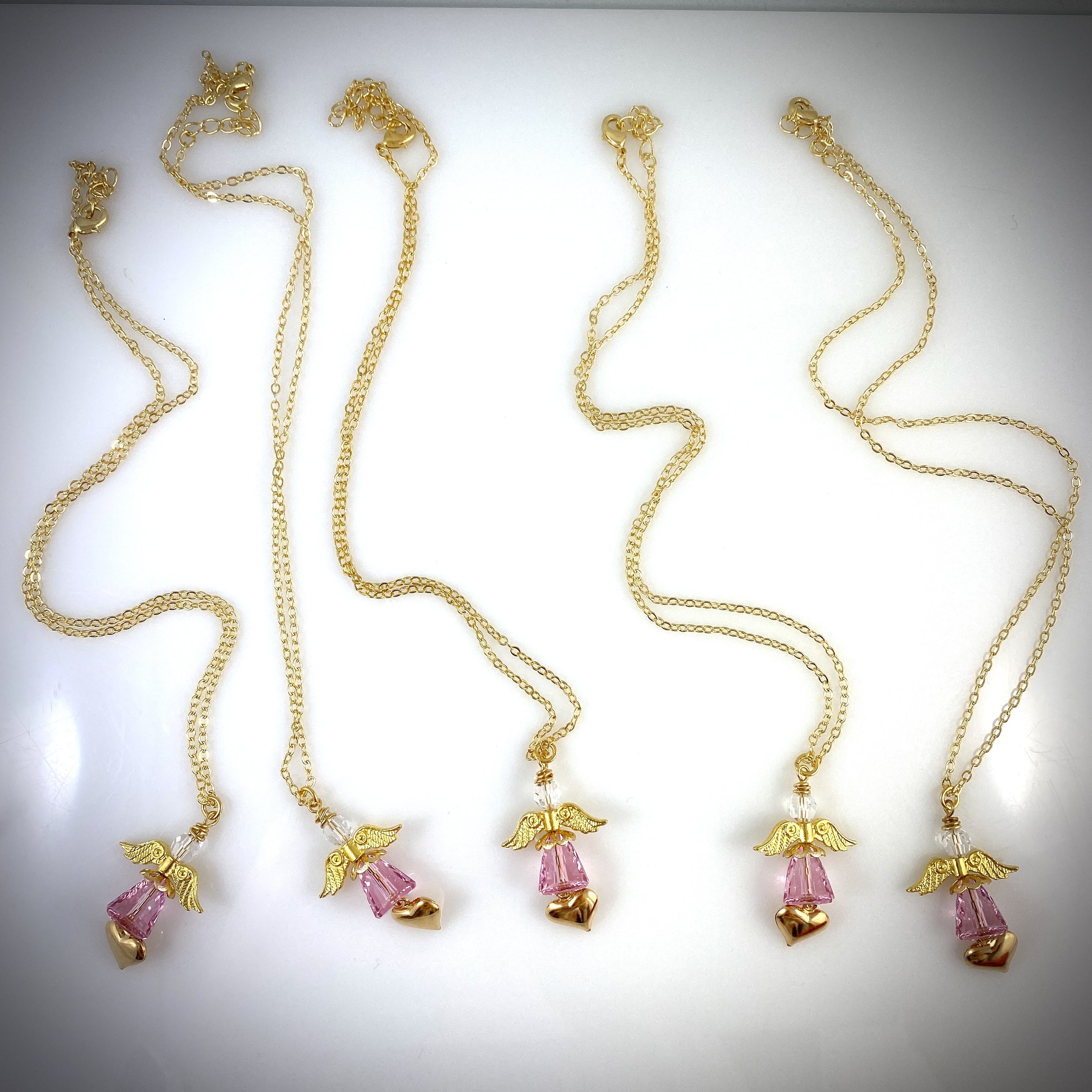 Small light pink angels with heart charms on golden necklace chains