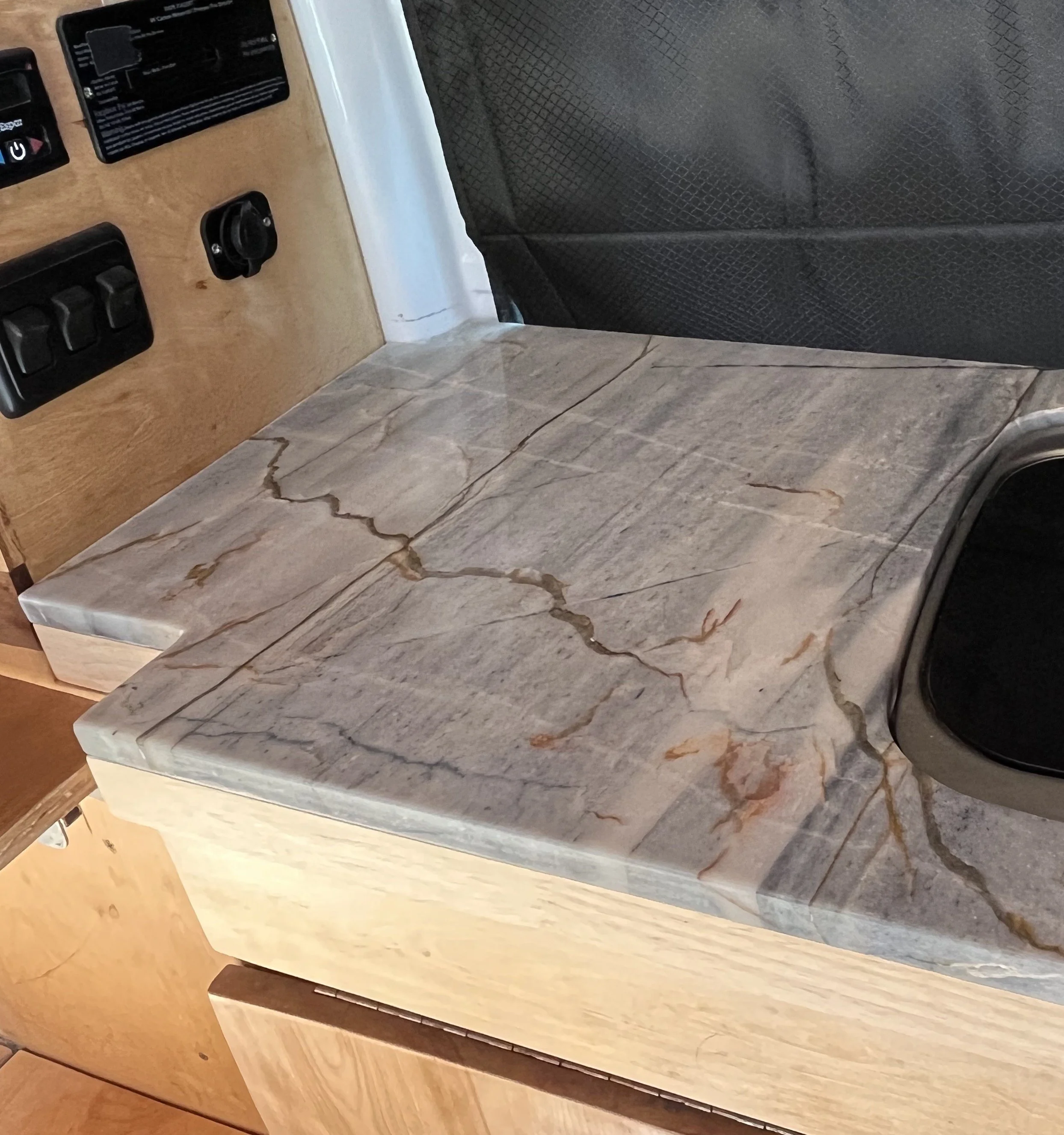 A kitchen countertop made of gray marble with brown and white veining, mounted on light wood cabinetry.