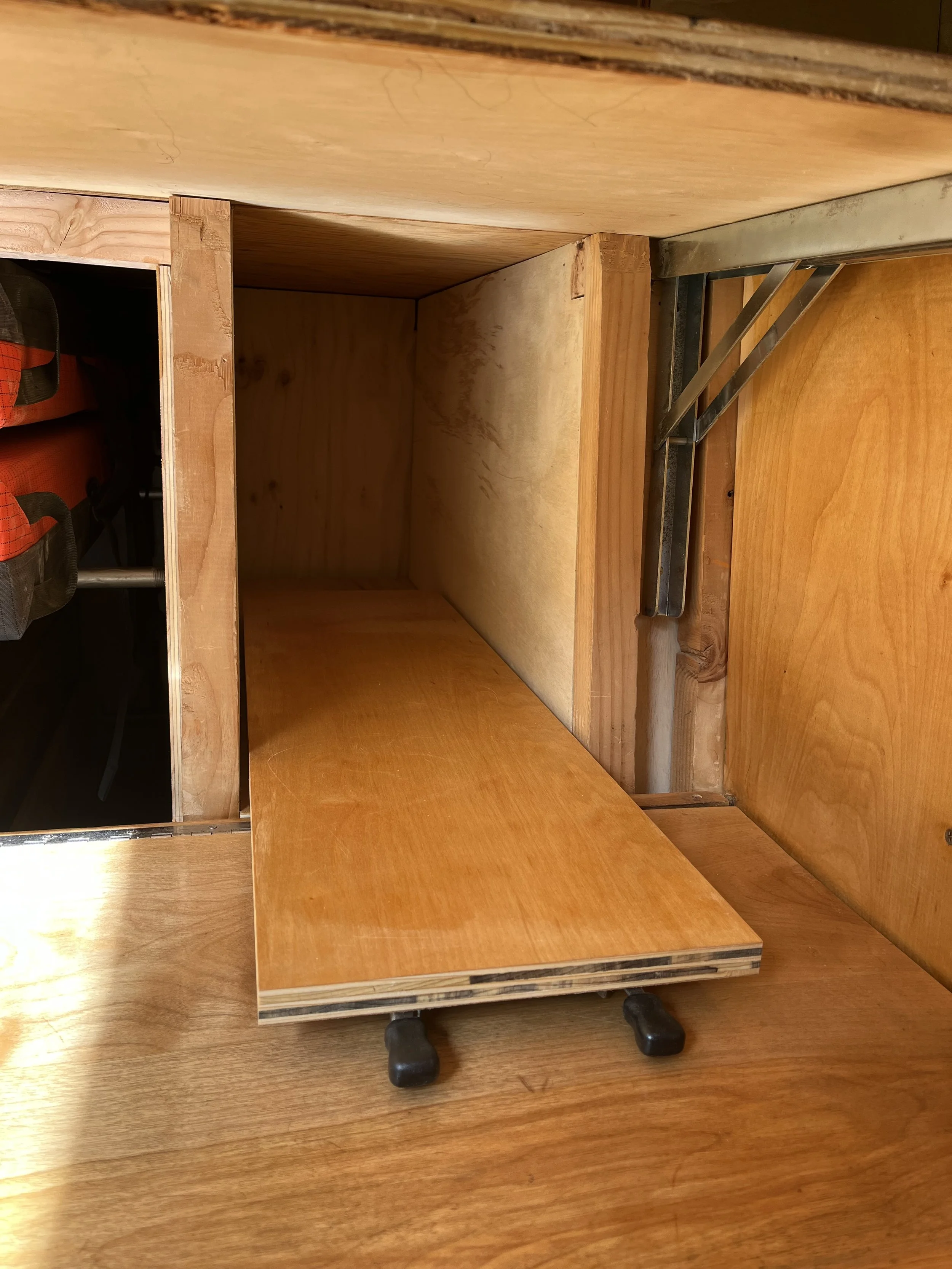 Interior of a wooden desk or cabinet with a sliding drawer on wheels and some metal support brackets.