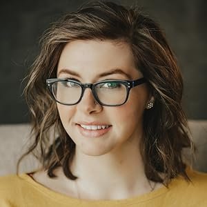A young woman with brown hair, glasses, and earrings, smiling at the camera.
