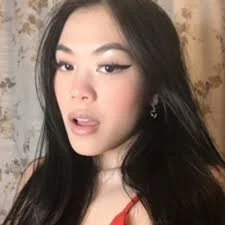 A young woman with long dark hair and makeup, wearing earrings and a red top, looking at the camera.