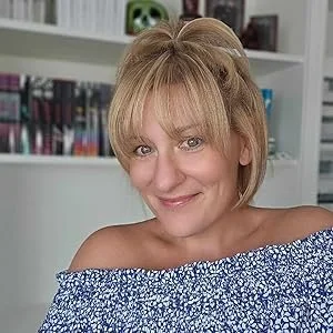 A woman with short blonde hair smiling in front of a bookshelf.