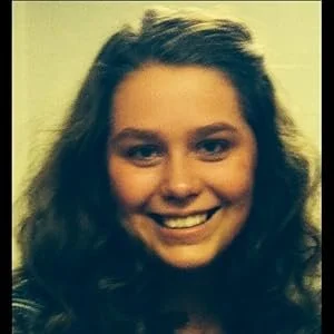 A young woman with curly brown hair smiling at the camera.