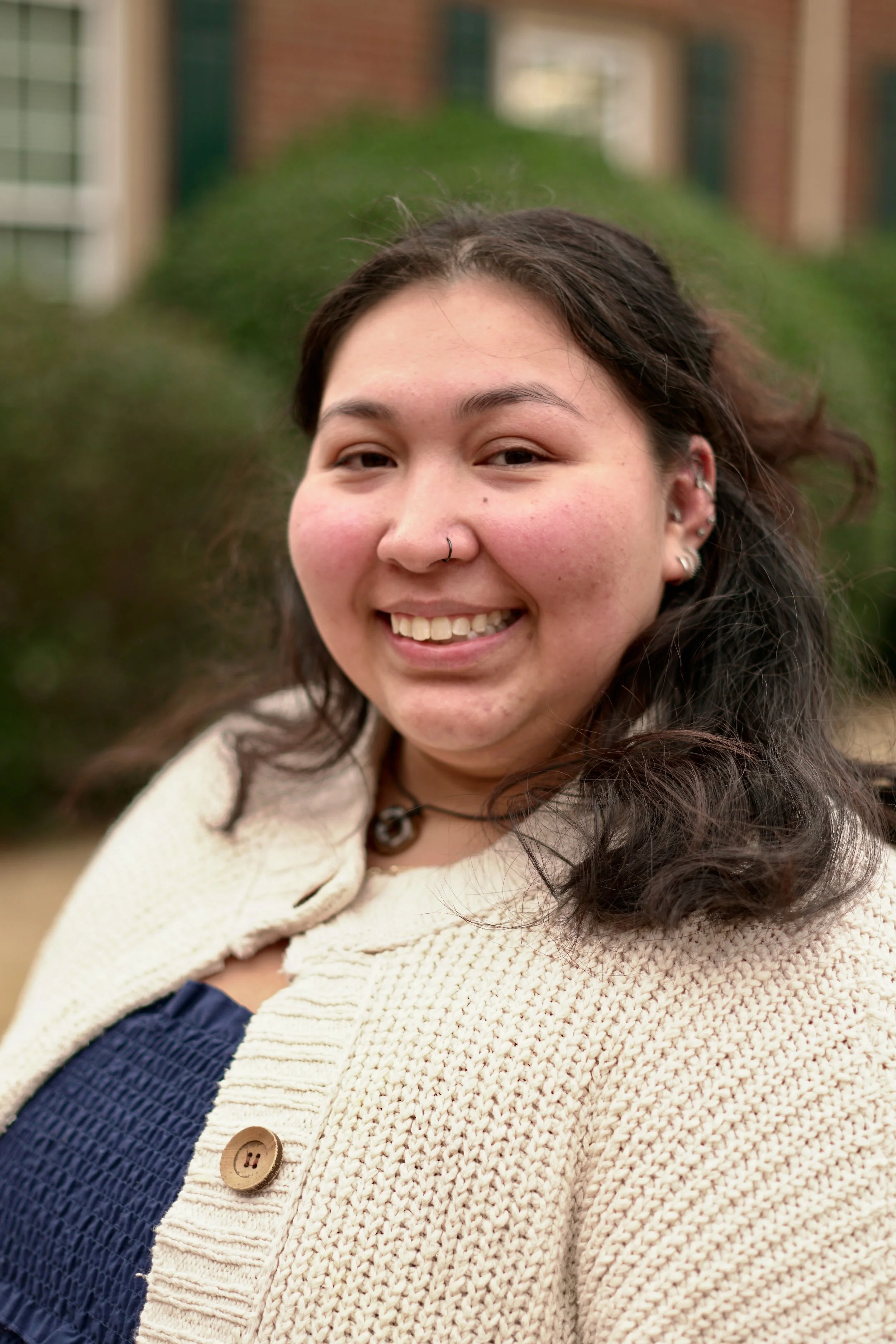 Close up image of a hispanic female smiling in front of a building and bush