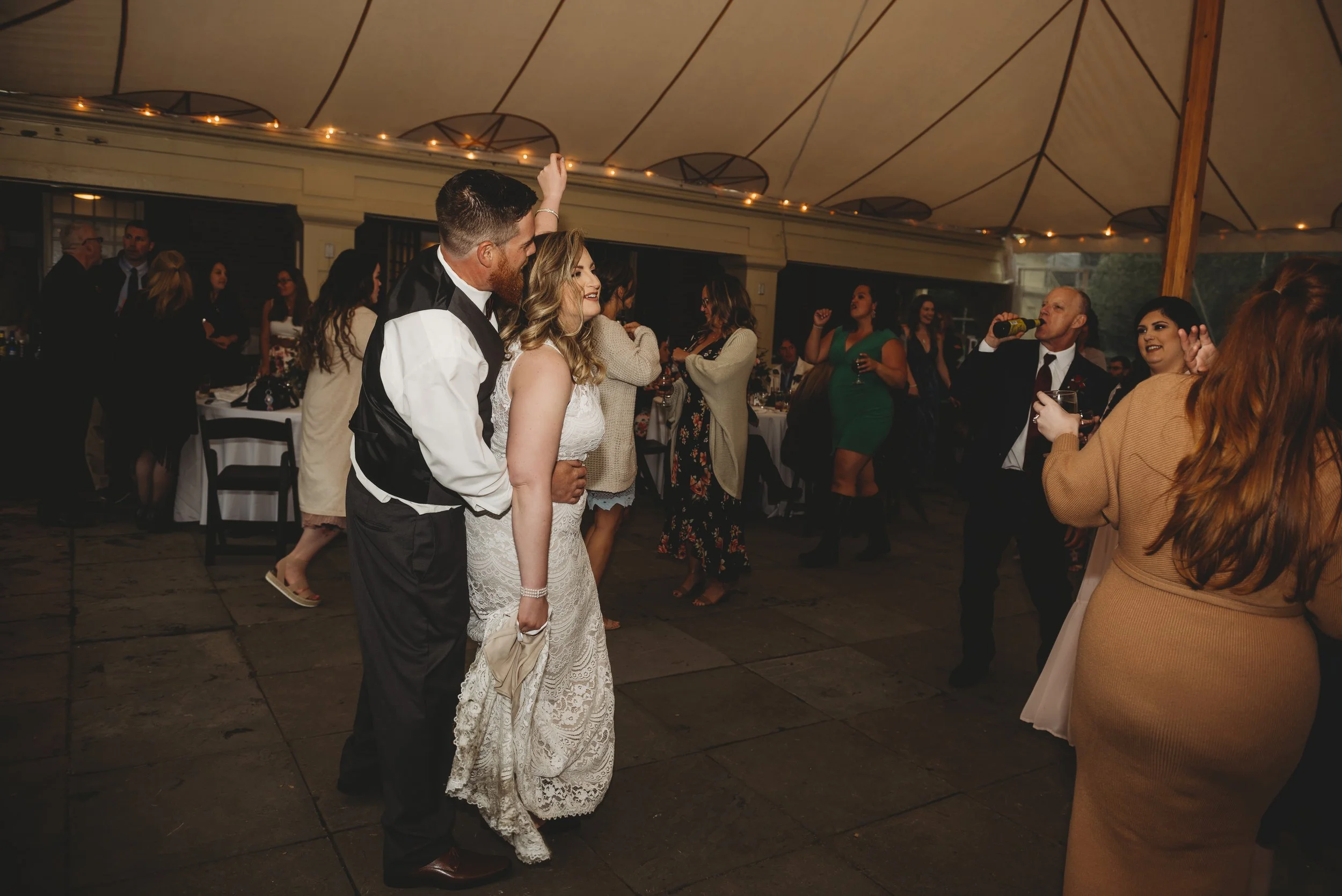 People dancing and socializing at a wedding reception inside a decorated tent.