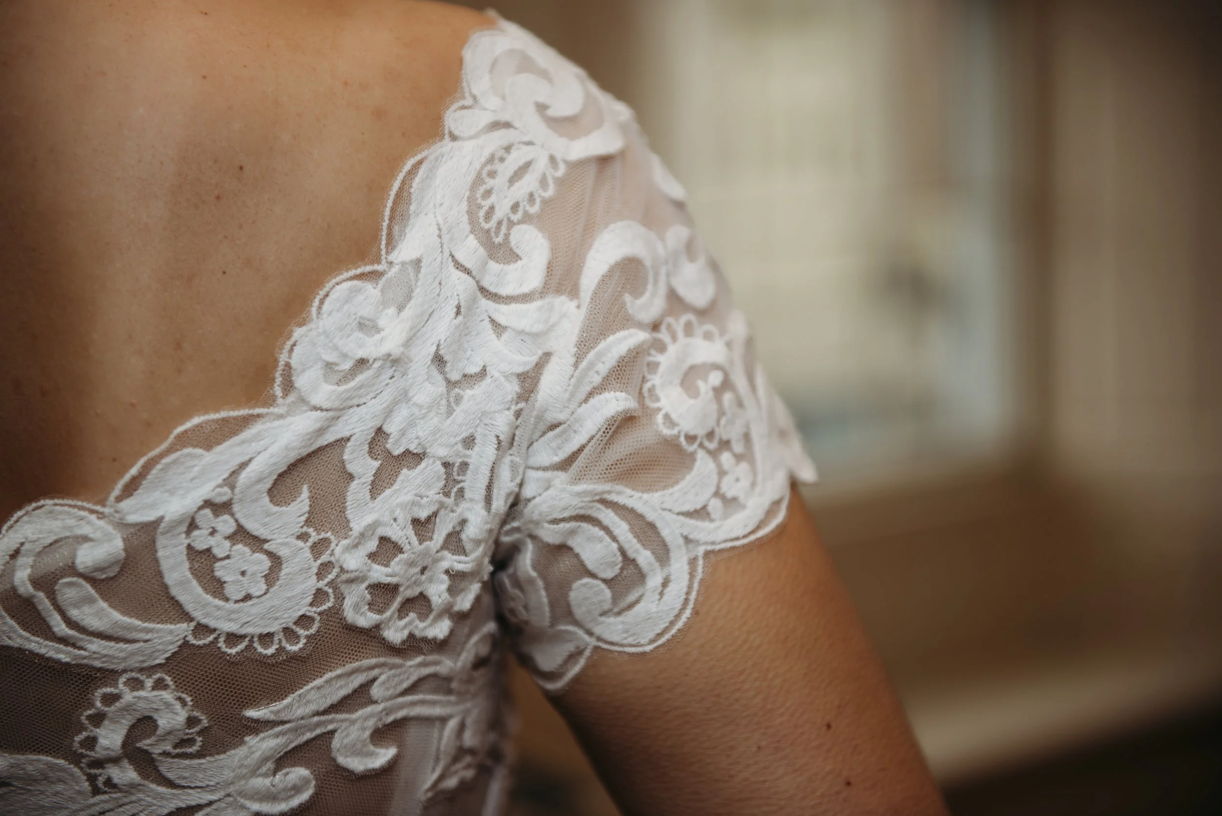 Close-up of a person wearing a white lace wedding dress with intricate embroidery on the shoulder and upper arm.