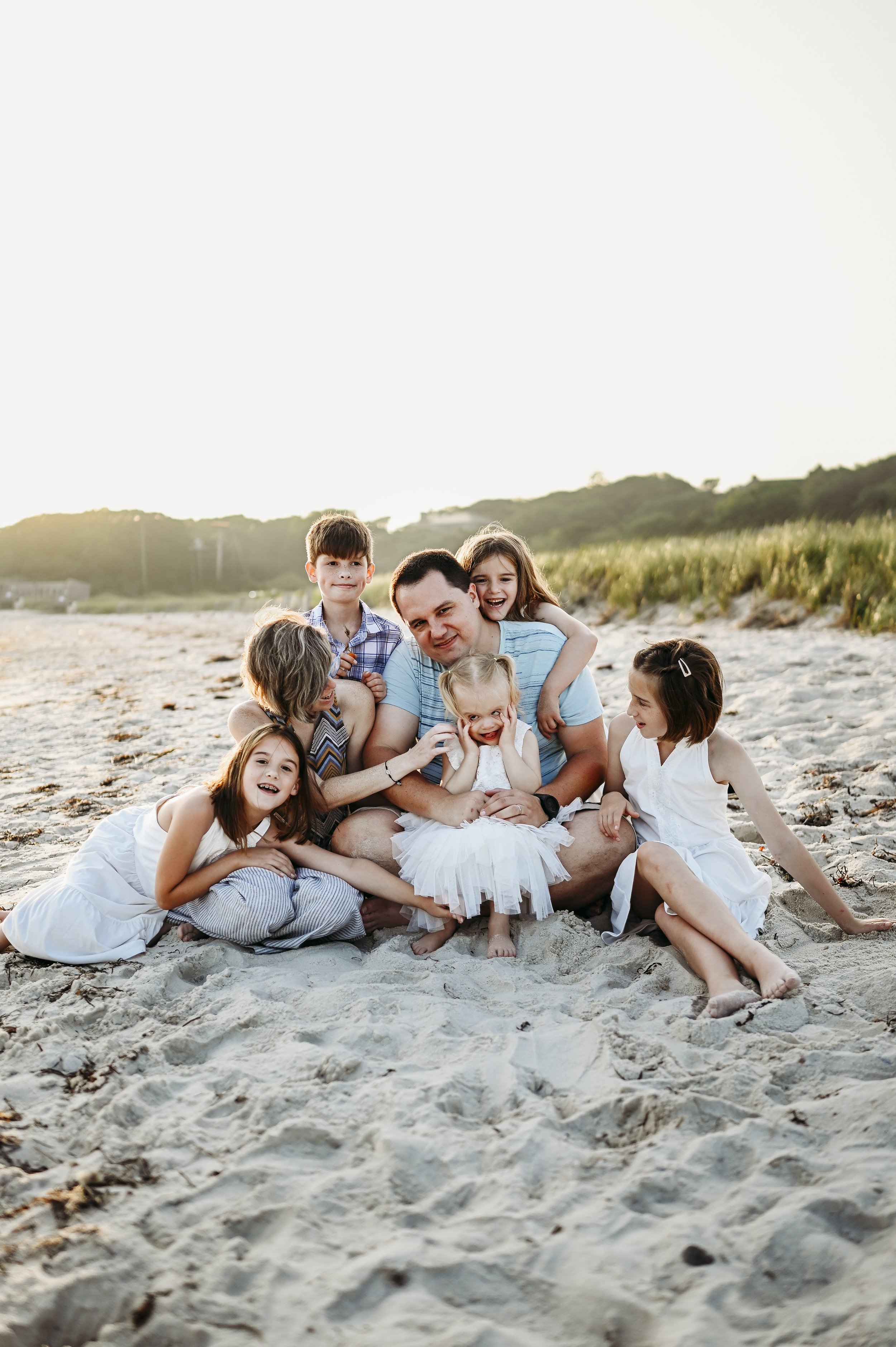 Family of seven with five children happily sitting on the beach at sunset