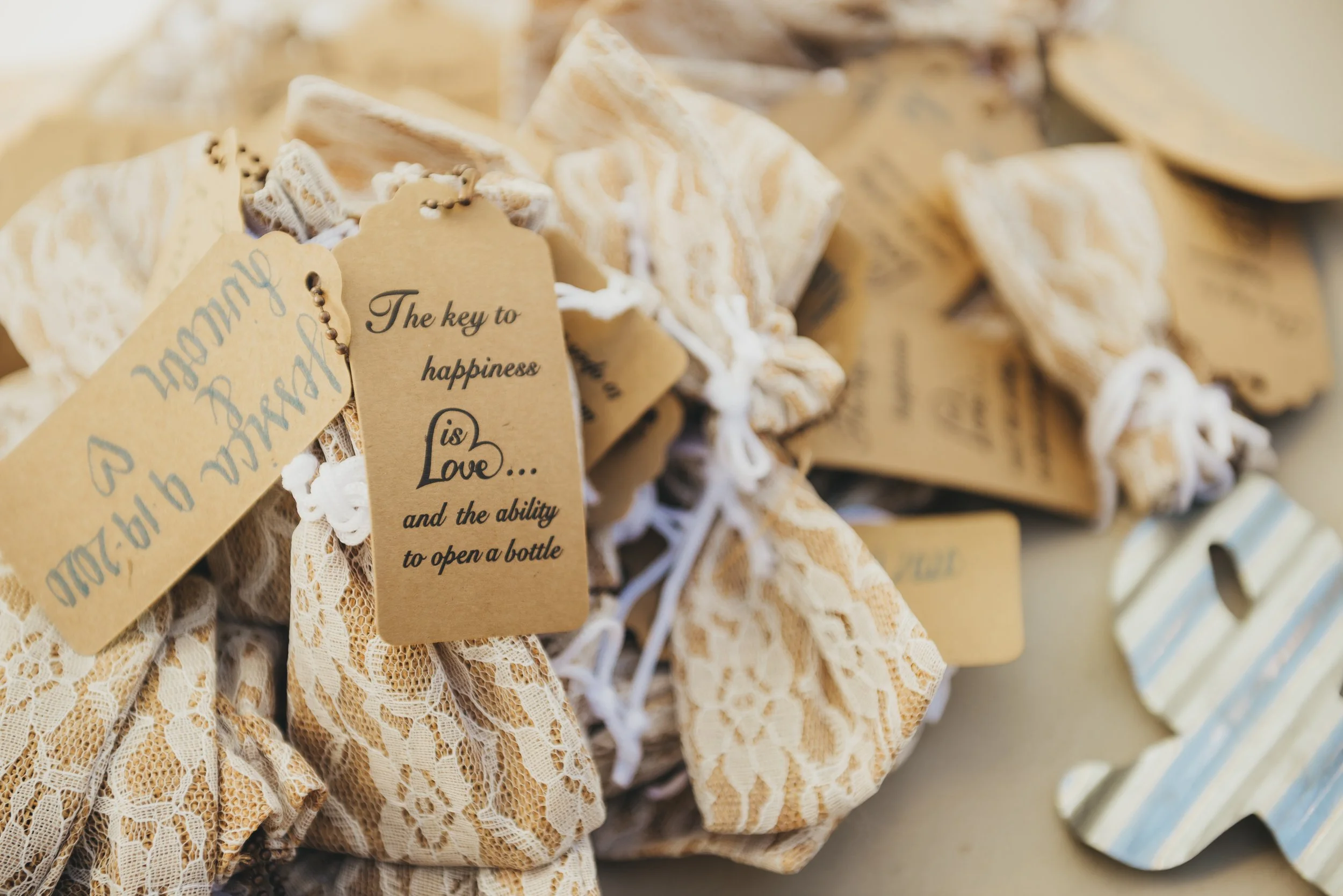 Small fabric gift bags tied with white string, each with a tan tag that reads "The key to happiness is Love... and the ability to open a bottle".