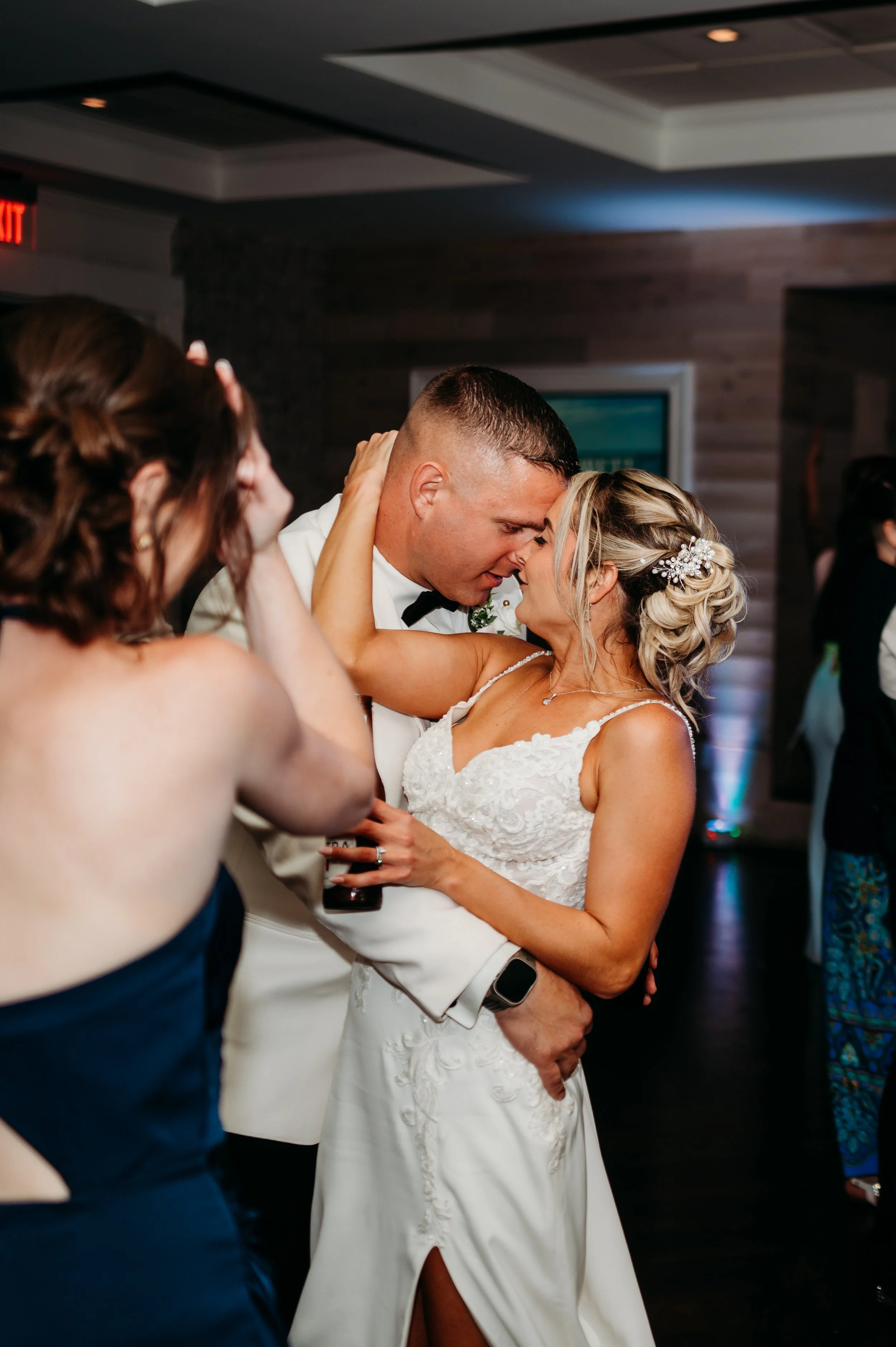 A bride and groom share a dance and kiss at their wedding reception, surrounded by guests.