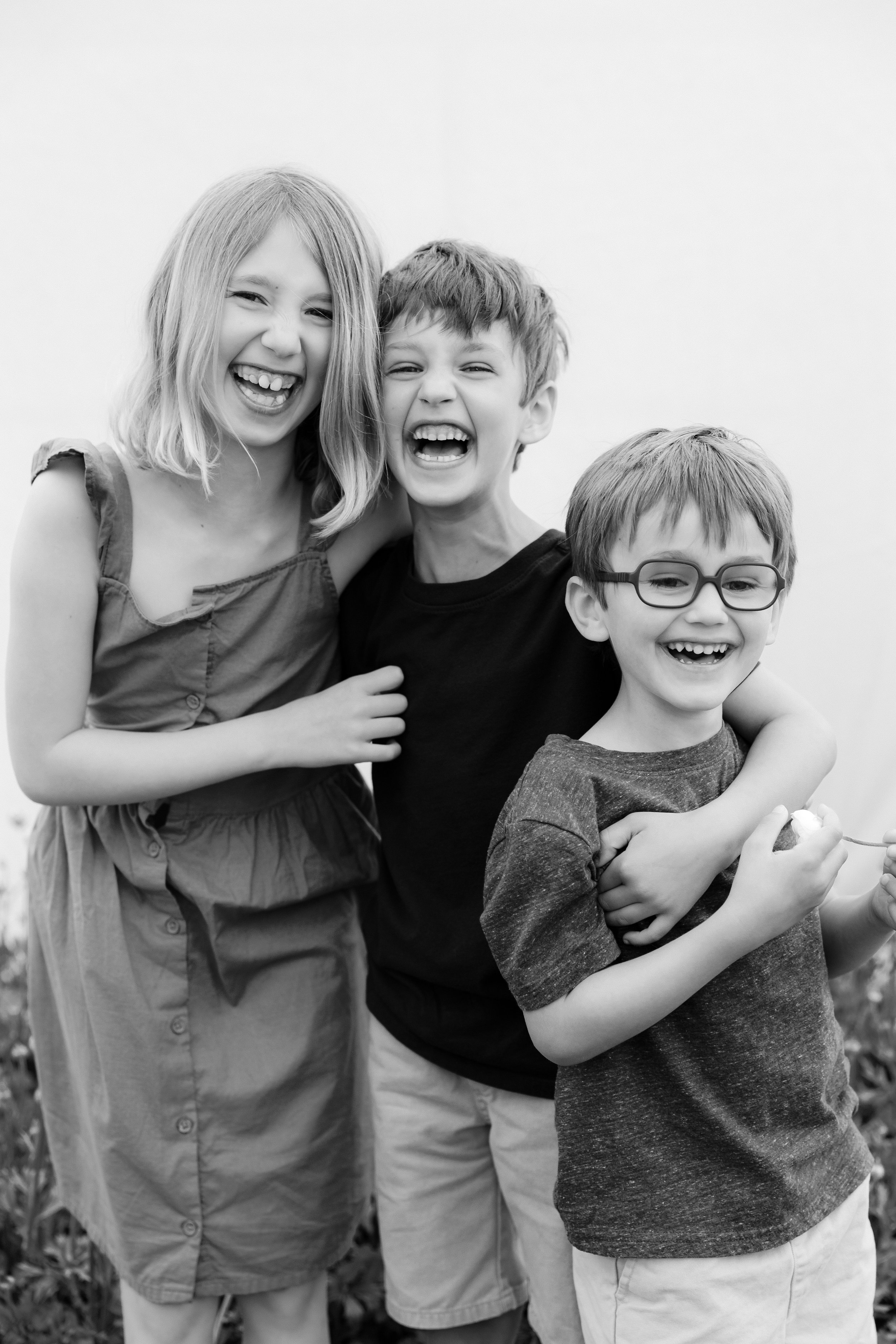 Black and white family photo of three children laughing and hugging together during an outdoor session in Rochester, NY.