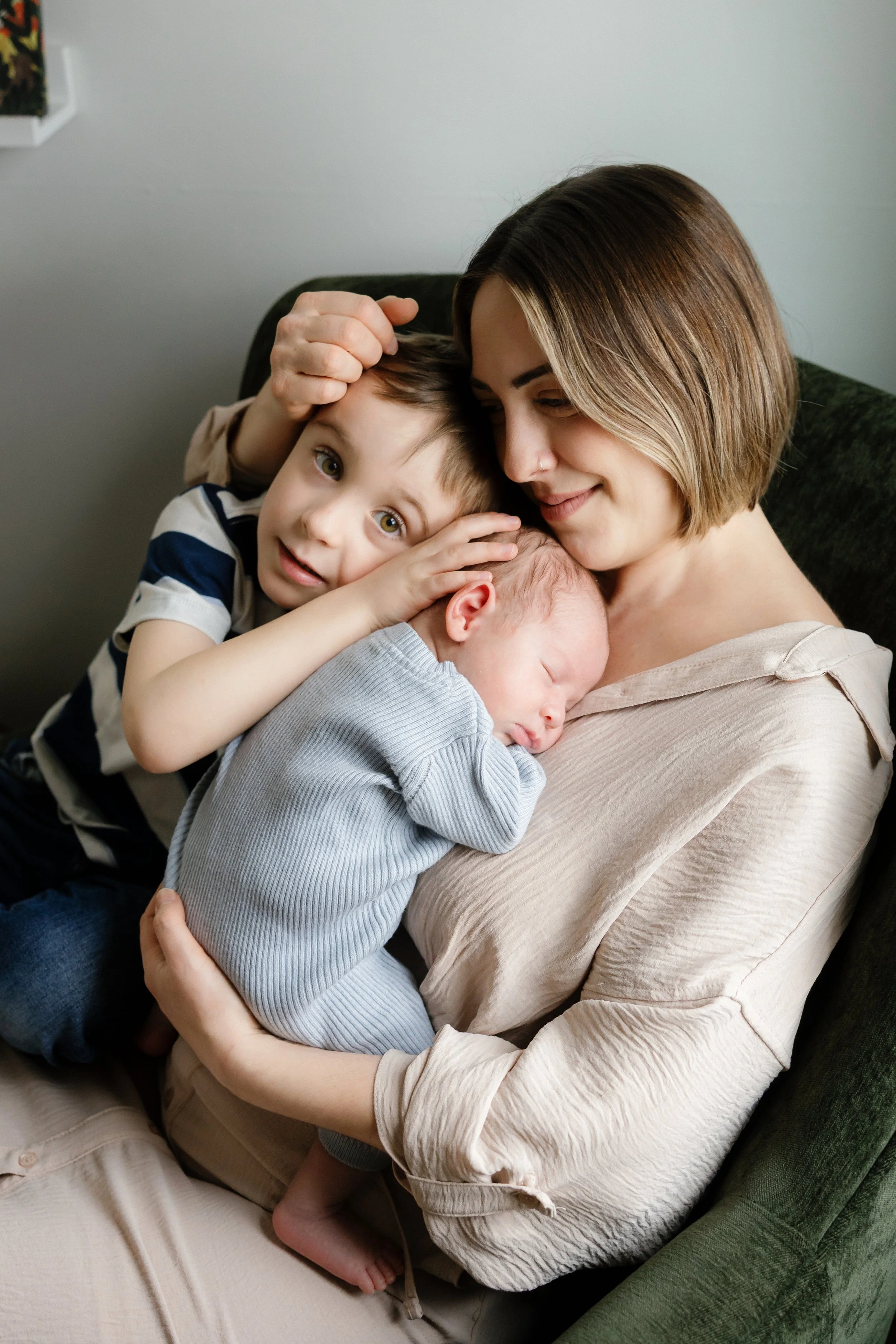 In-home newborn photo of a mother cuddling her children on a couch during a lifestyle family session in Rochester, NY.