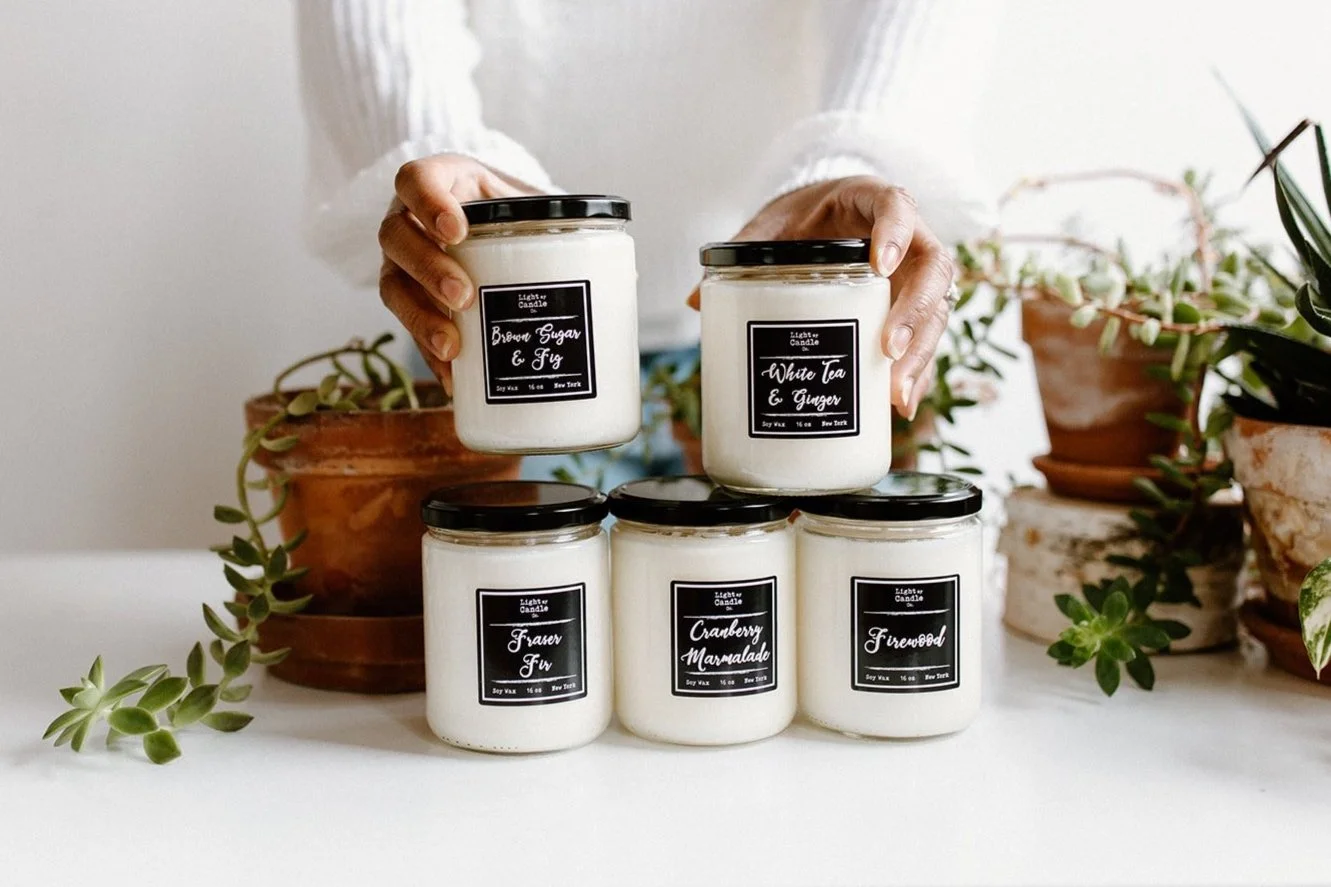 Product photo for Light My Candle Co featuring six white candles in glass jars arranged among potted plants in Rochester, NY.