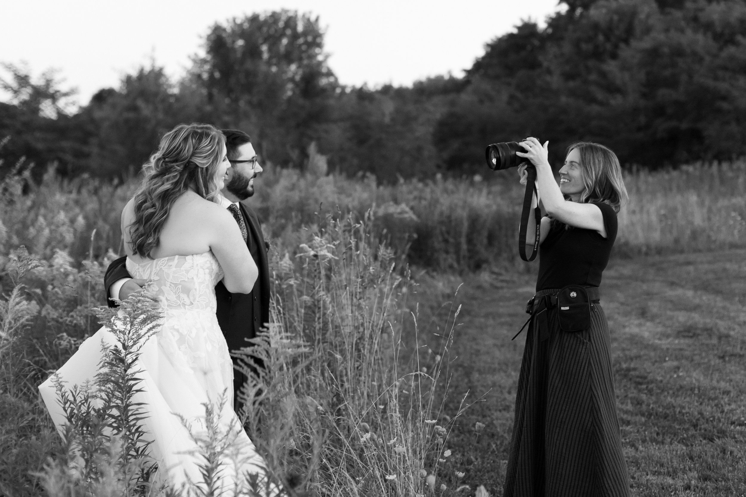 A couple is having their wedding photo taken outdoors in a grassy field near Seneca Lake, by Lindsay Stephany, a Rochester, NY photographer.