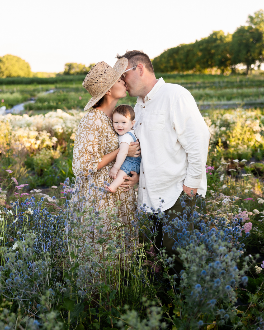 Family photo during a Flower Session at Flowerwell, showing parents holding their baby in a blooming flower field in Rochester, NY.