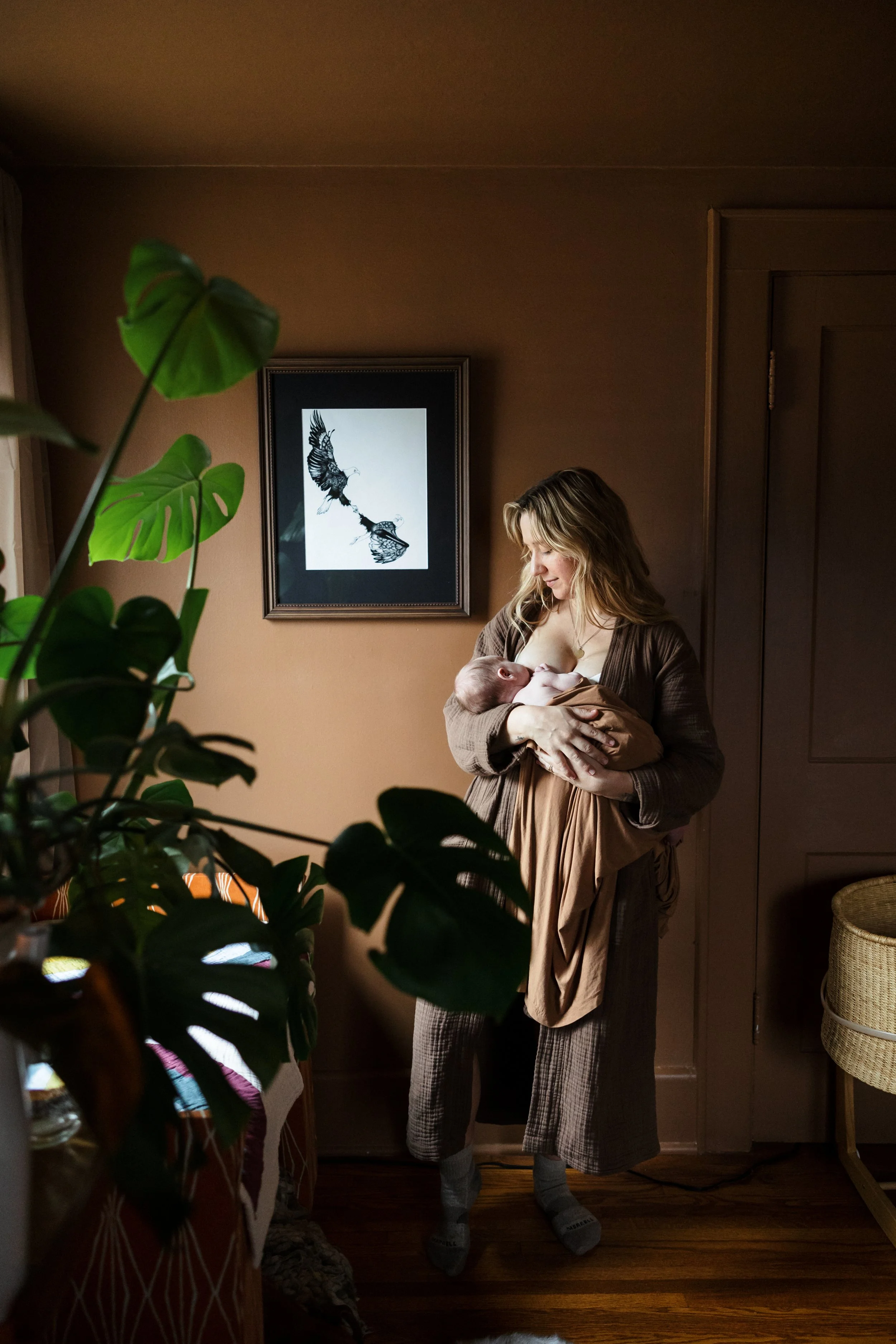 A woman cradling a newborn baby indoors during a cozy  in-home newborn session in Rochester, NY.