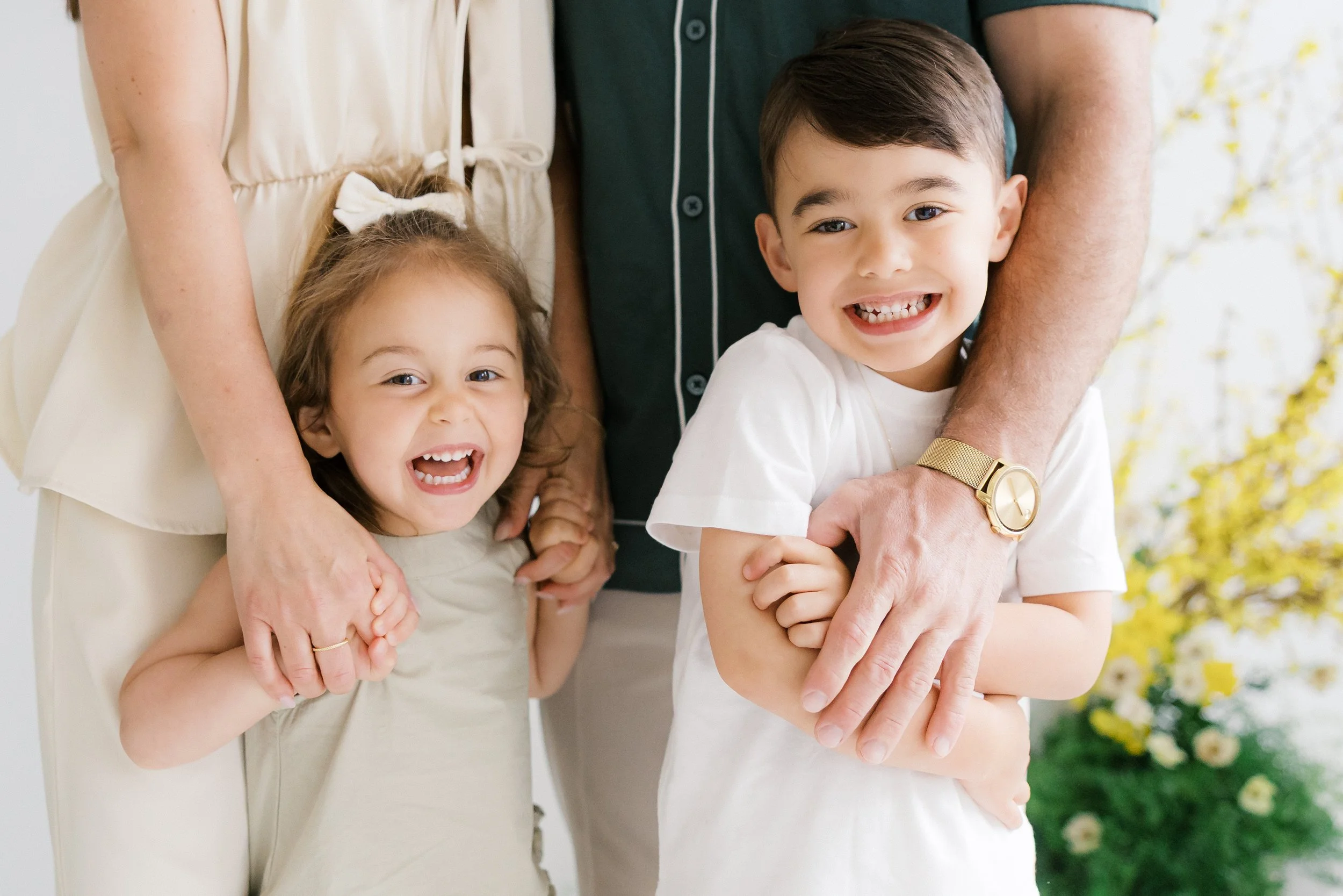 Close-up of happy young siblings, girl and boy, being held by their parents during a studio family session in Rochester, NY.