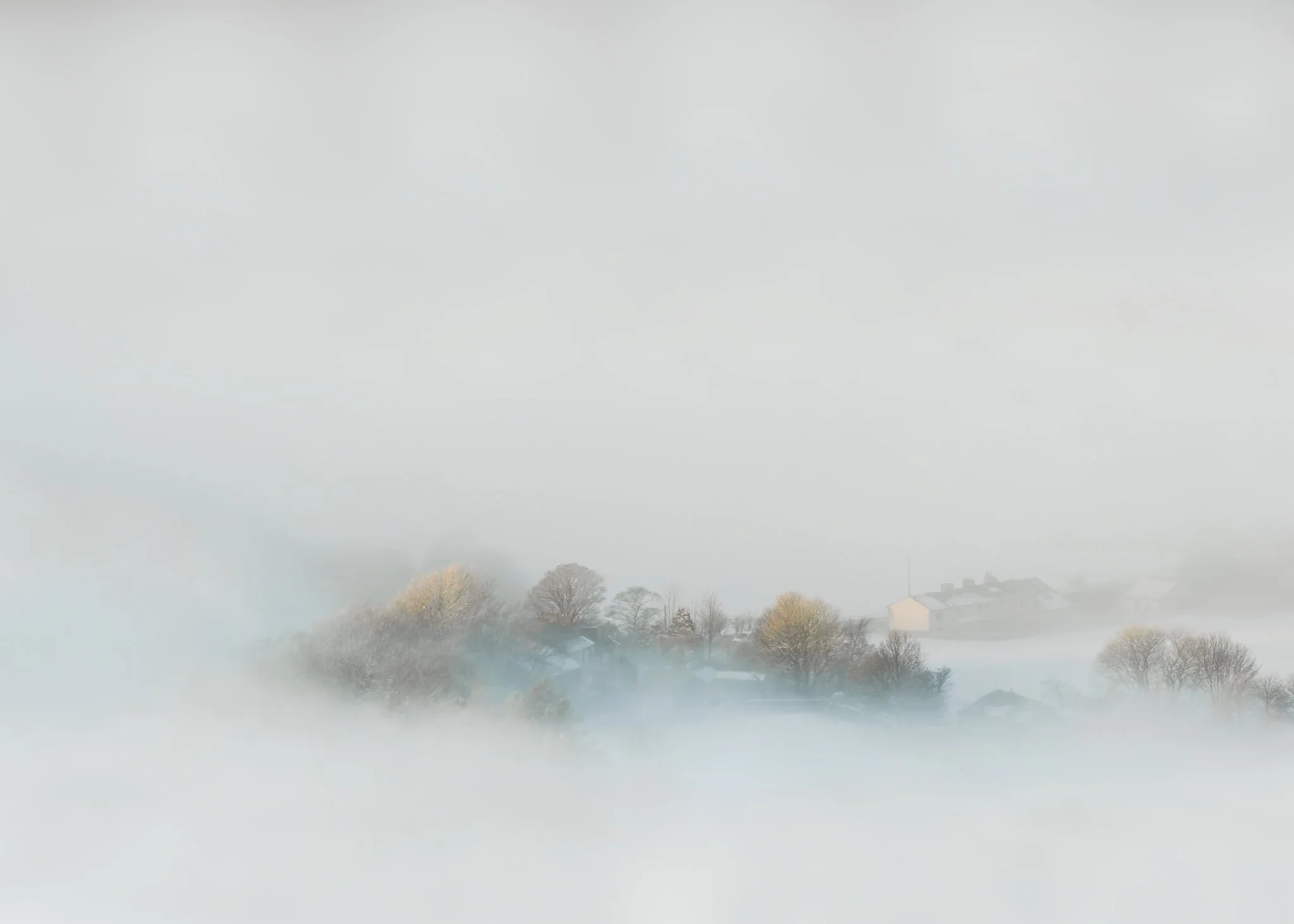 Turn Village, Rossendale, surrounded by snow and fog — the clustered rooftops nestle in the folds of a valley, fading into mist.