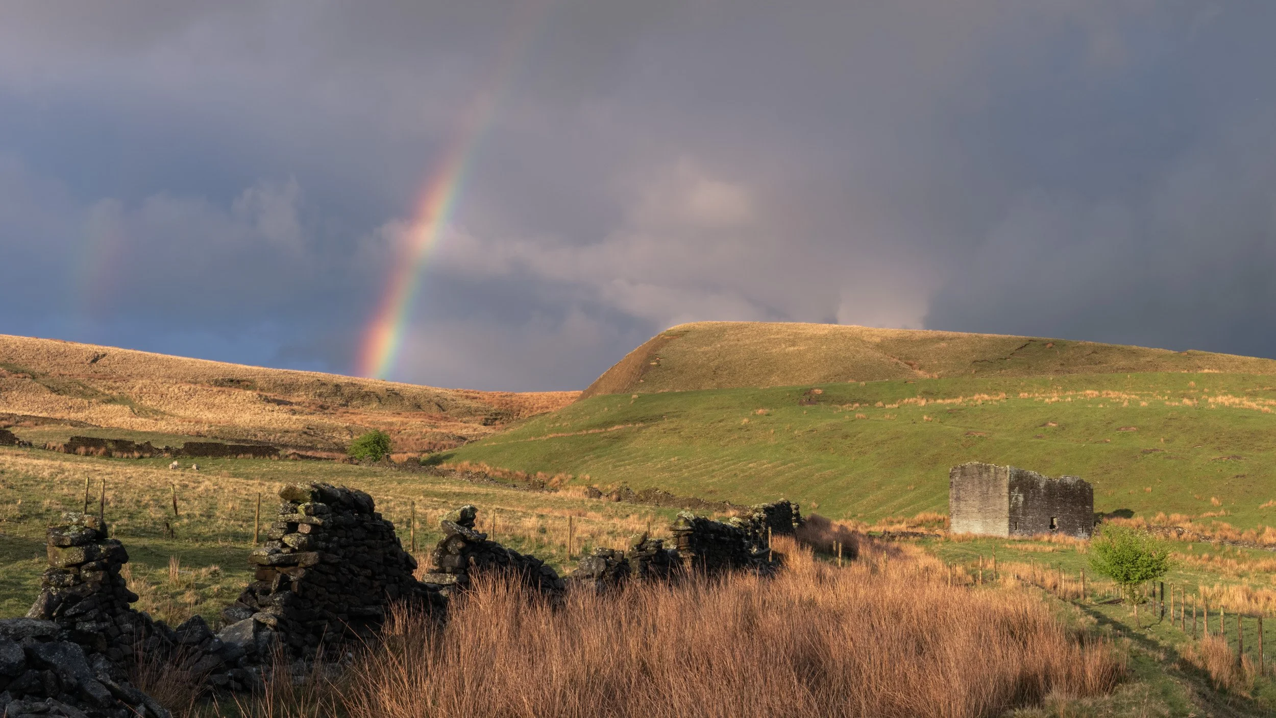 Vibrant rainbow arching over ruined stone walls and an old deralict stone barn in Naden Valley near Scout Moor, Norden.