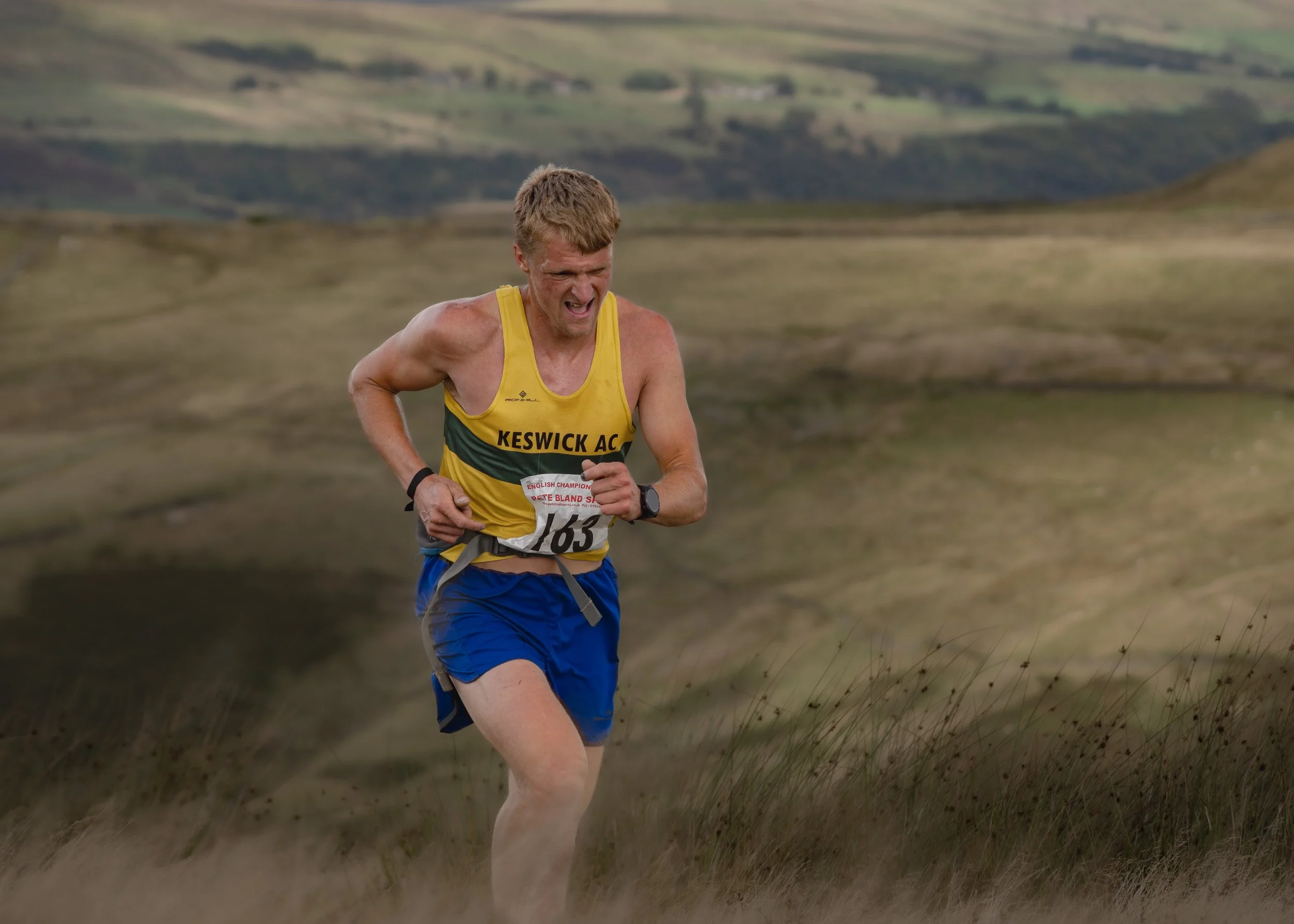 Keswick AC fell runner in a yellow and green vest grimacing as he sprints uphill during the Whittle Pike race on Scout Moor.