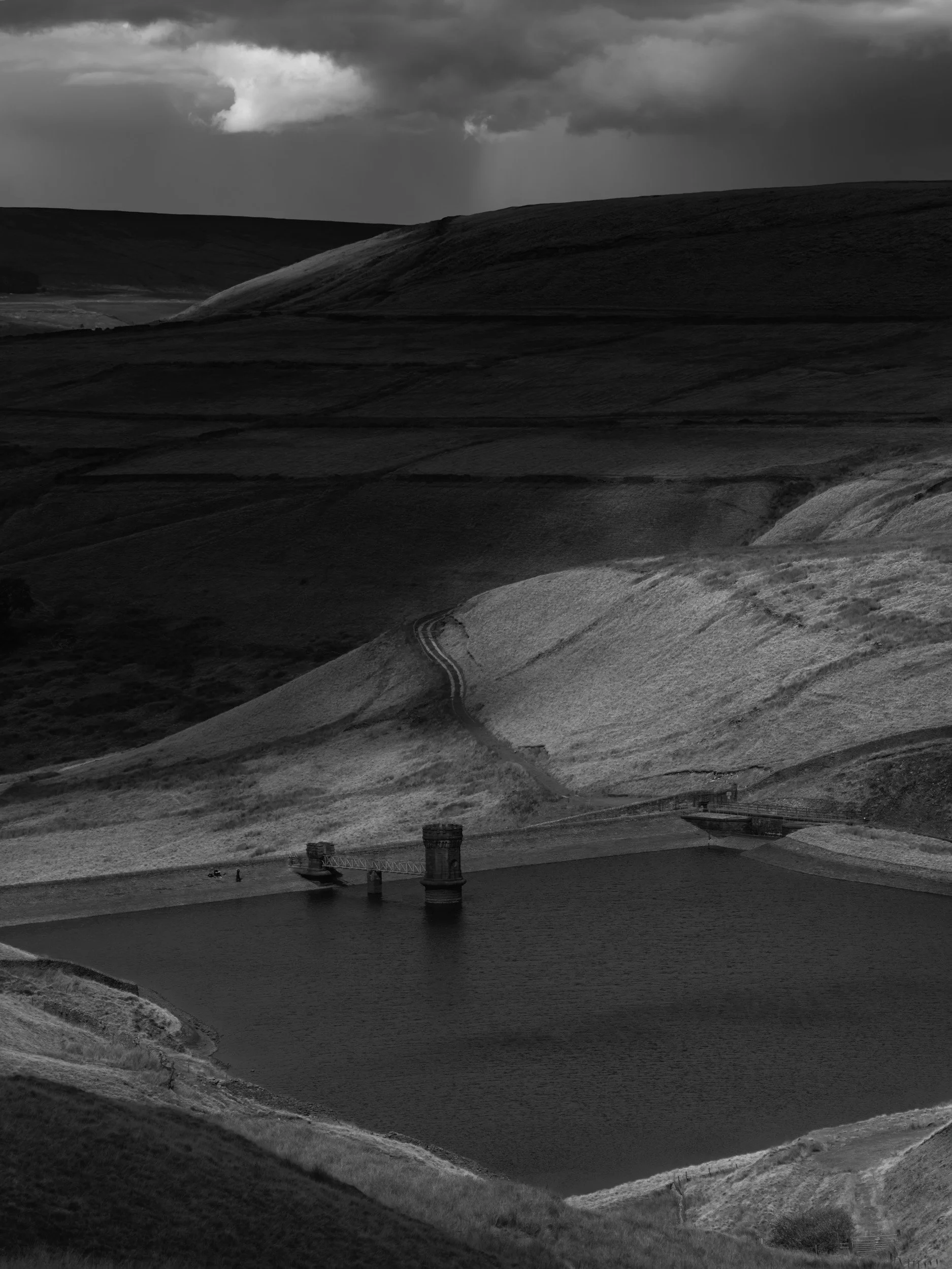High-contrast monochrome landscape of Scout Moor High Level Reservoir under dark, moody skies.