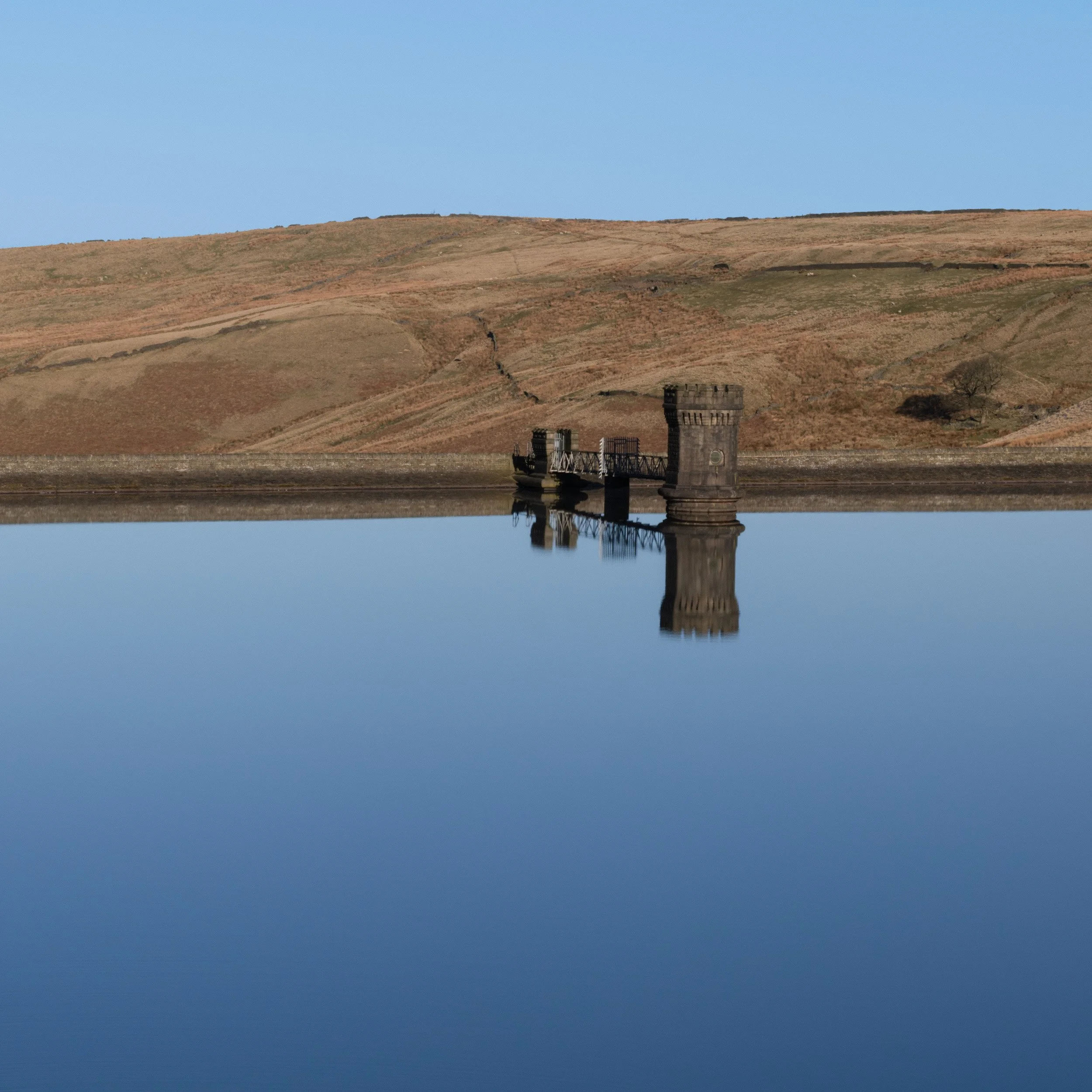 Symmetrical mirror reflection of the stone valve tower and blue sky in the glassy surface of Scout Moor High Level Reservoir.