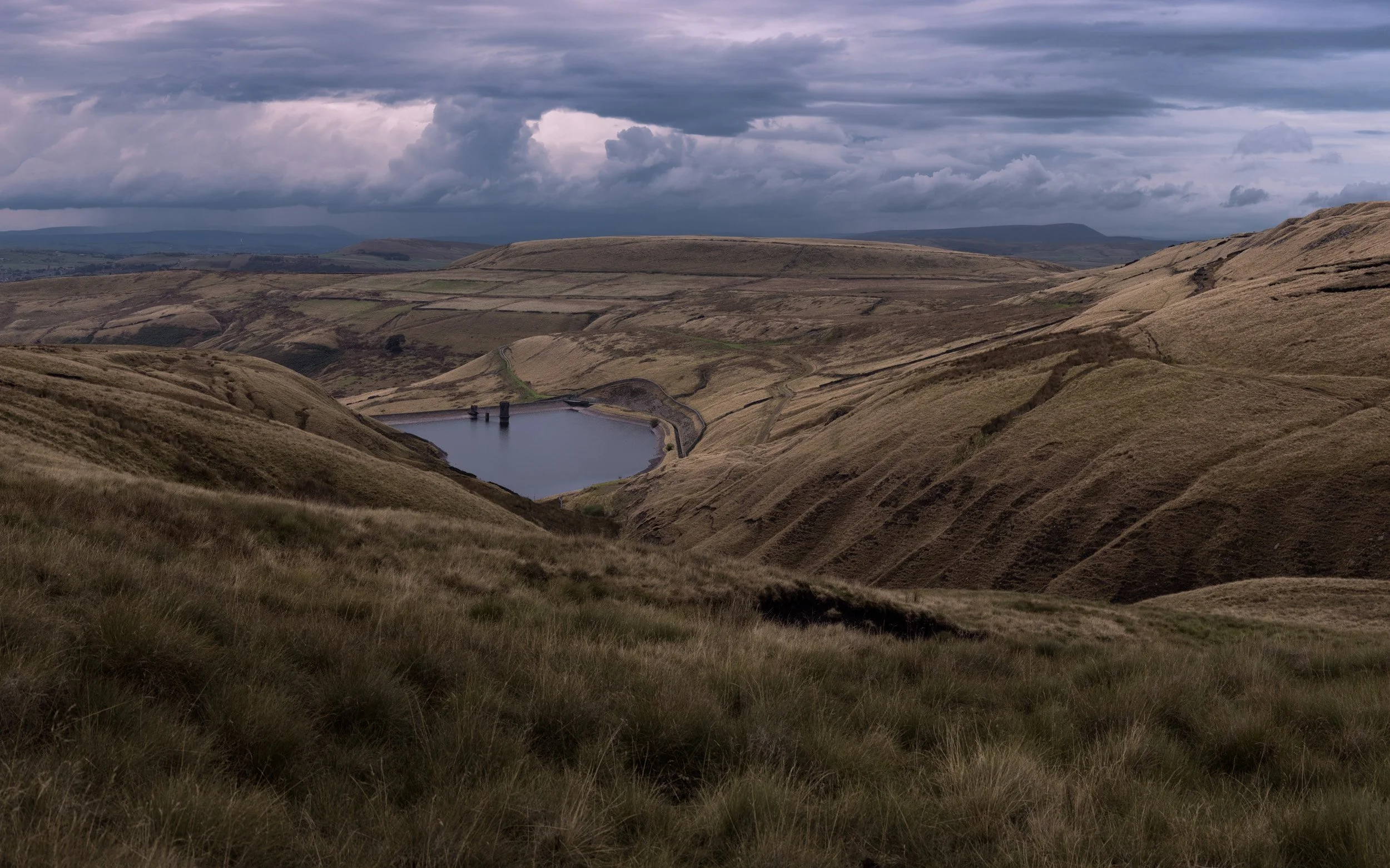 Break in dark clouds revealing a patch of light sky above Scout Moor High Level Reservoir and surrounding ridges.