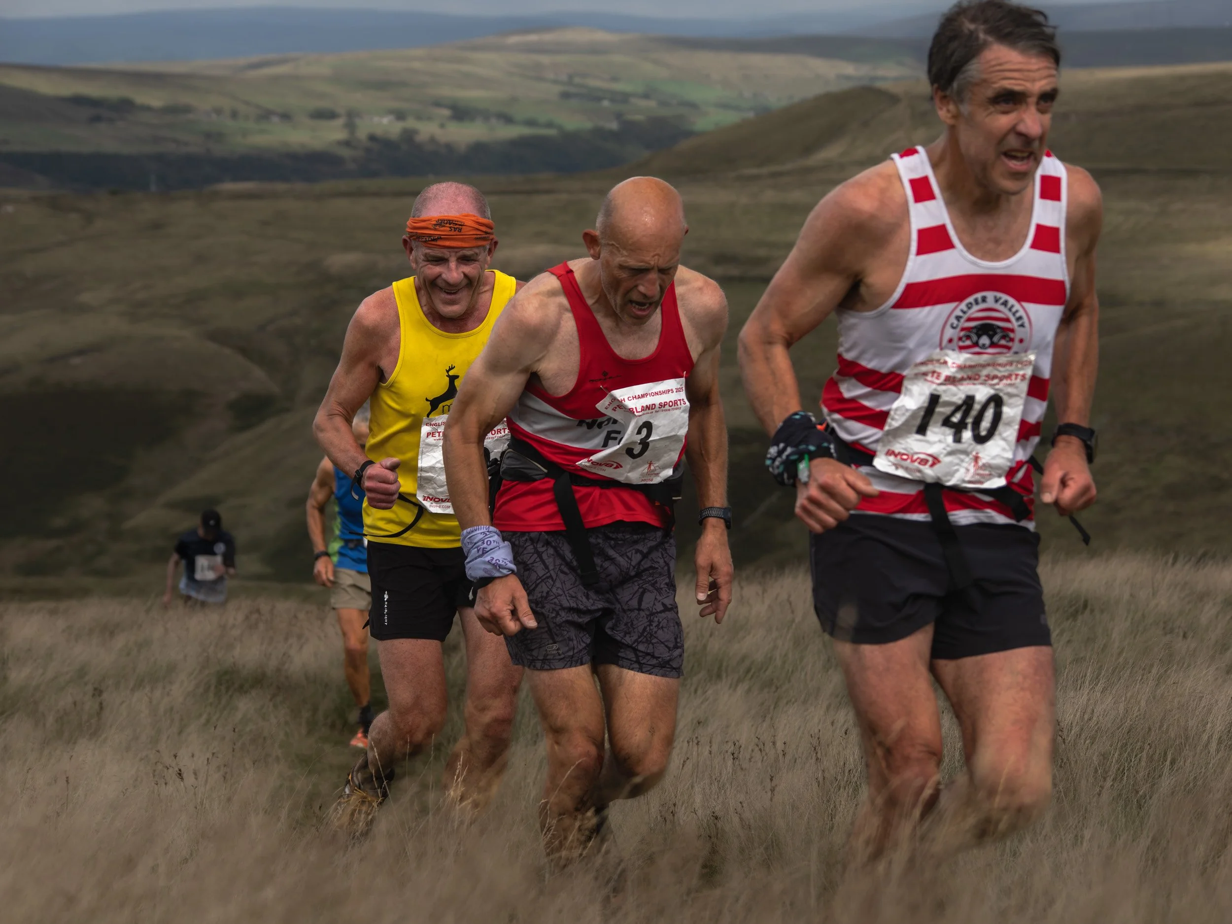 Pack of veteran fell runners, including Calder Valley (#140), working together up a steep slope on Scout Moor.