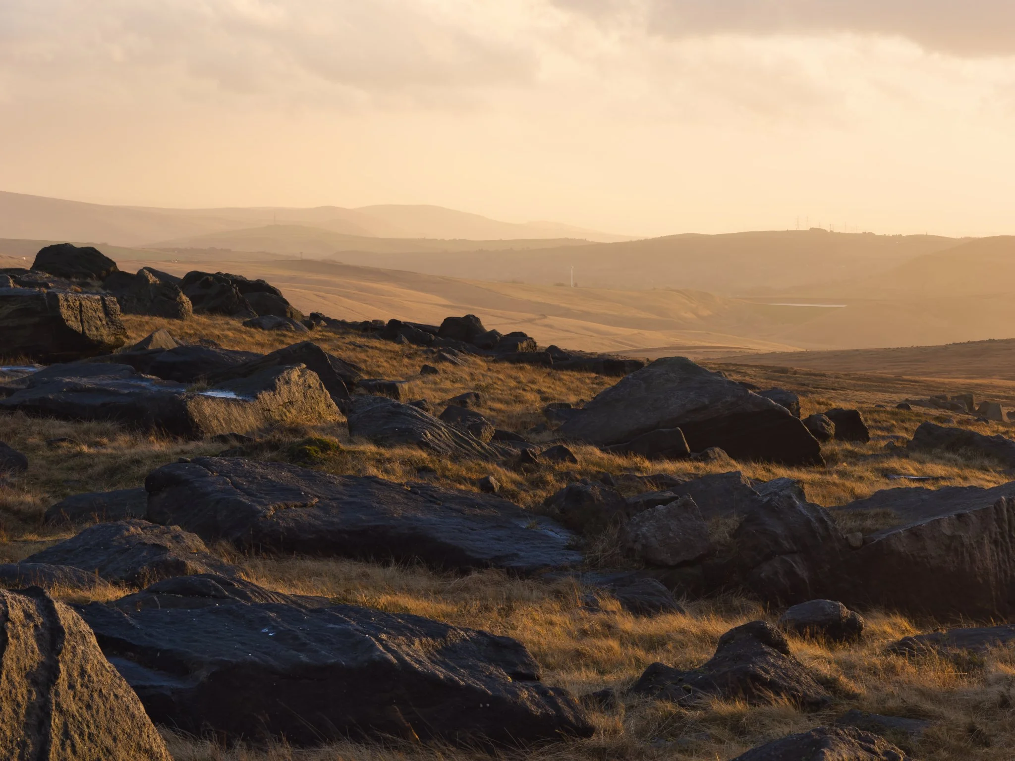 Blackstone Edge — a dramatic boulder field punctuated by rocky outcrops and distant hills during a hazy sunset.