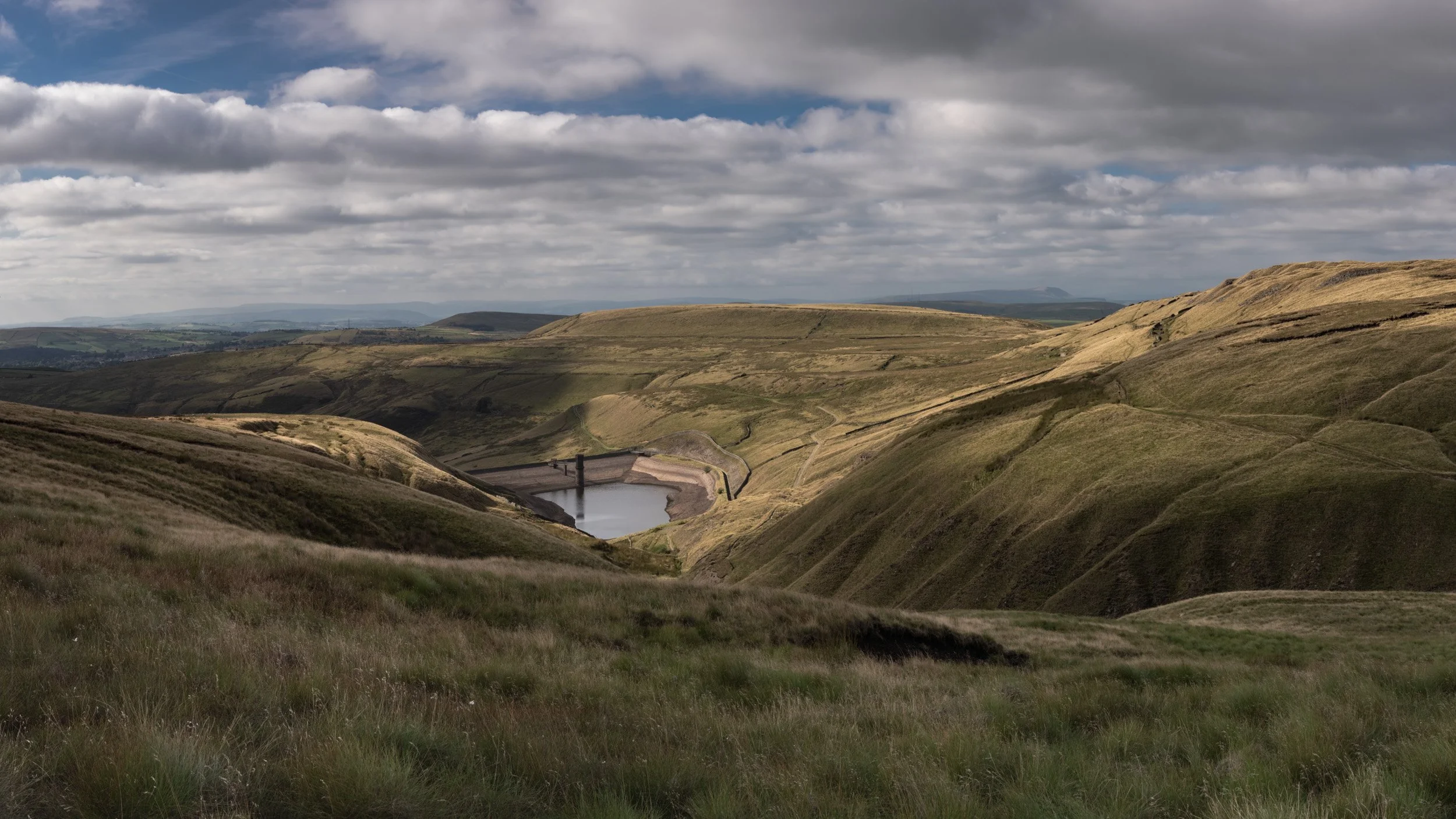 Wide panorama of Scout Moor High Level Reservoir with dappled sunlight highlighting the surrounding green valleys.