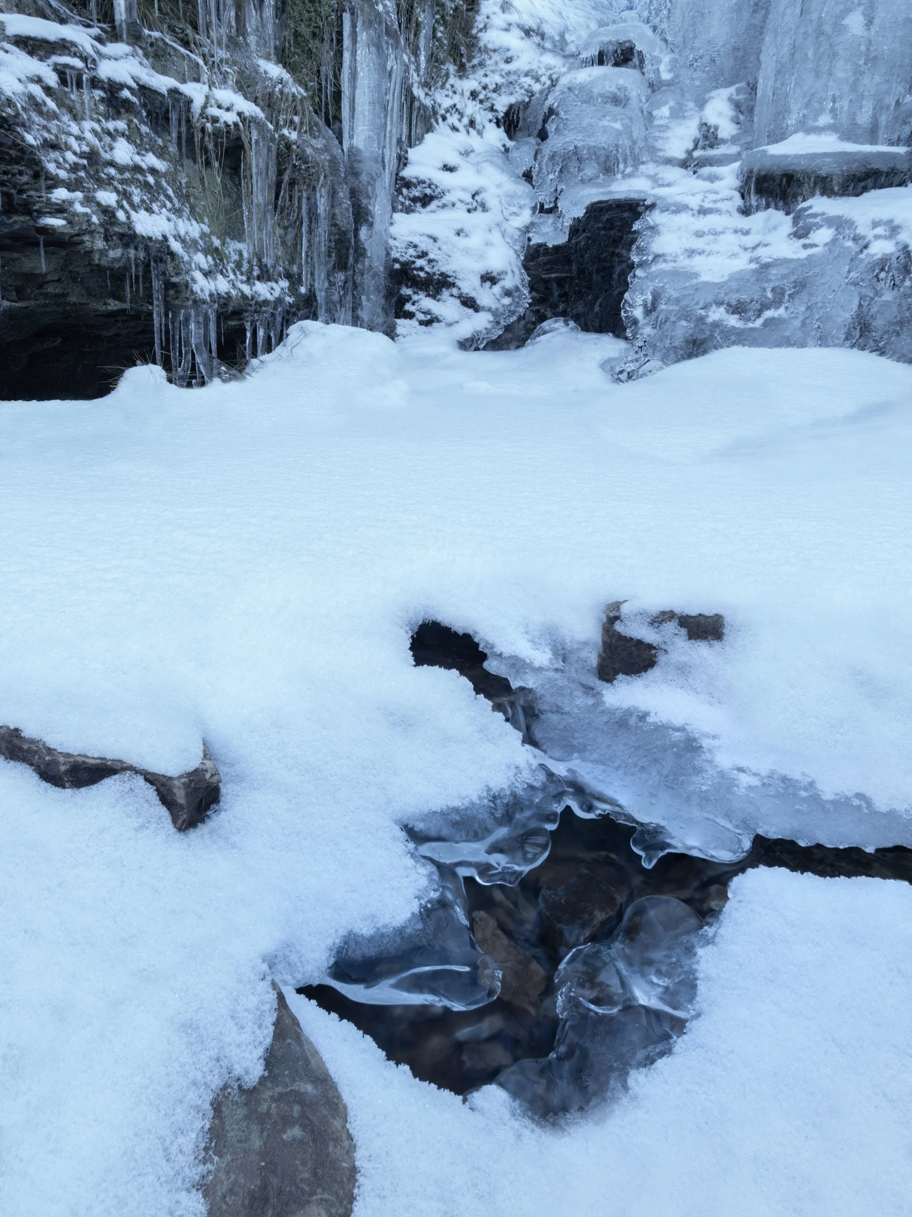 Frozen stream and cascading icicles hanging over snow-covered rocks near Scout Moor High Level Reservoir, on Scout Moor, Rossendale