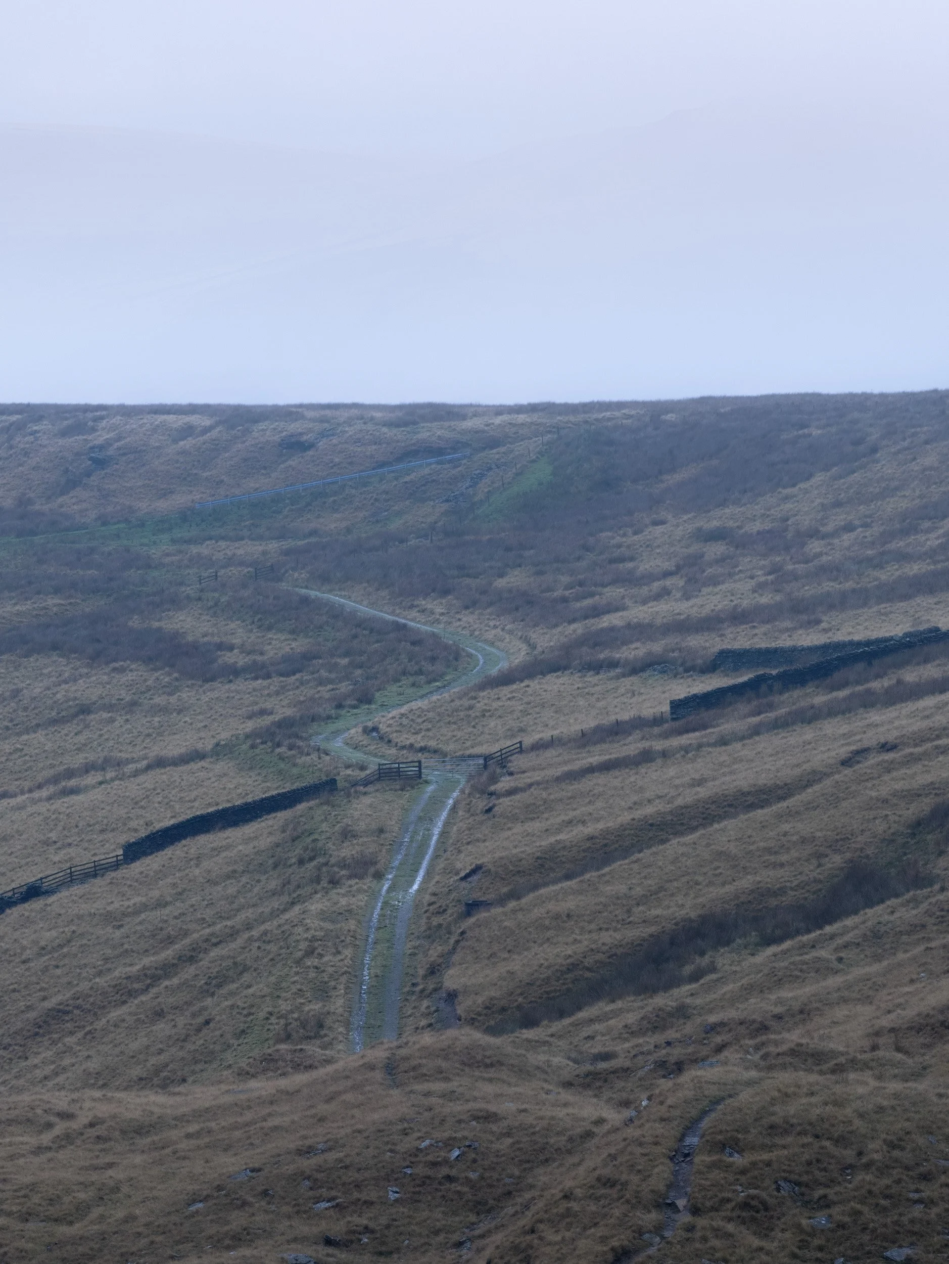Vertical telephoto shot of a winding gravel track and drystone wall cutting through muted moorland pastures on Scout Moor.