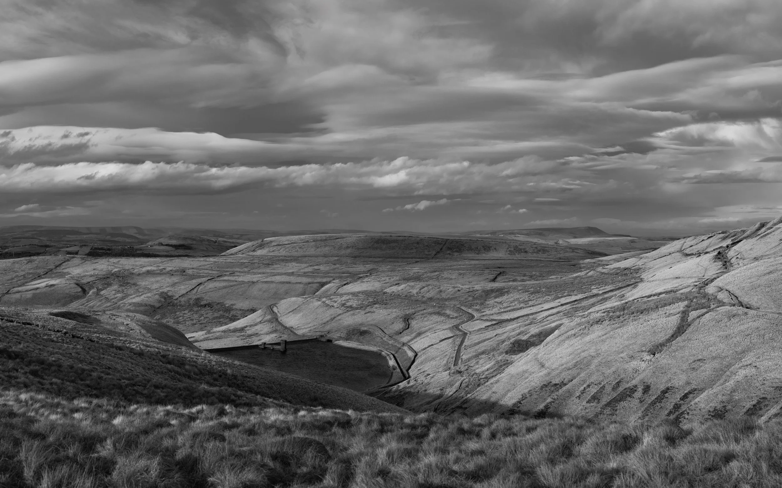 Black and white landscape photograph looking across the sweeping textures and valley contours of Scout Moor High Level Reservoir.