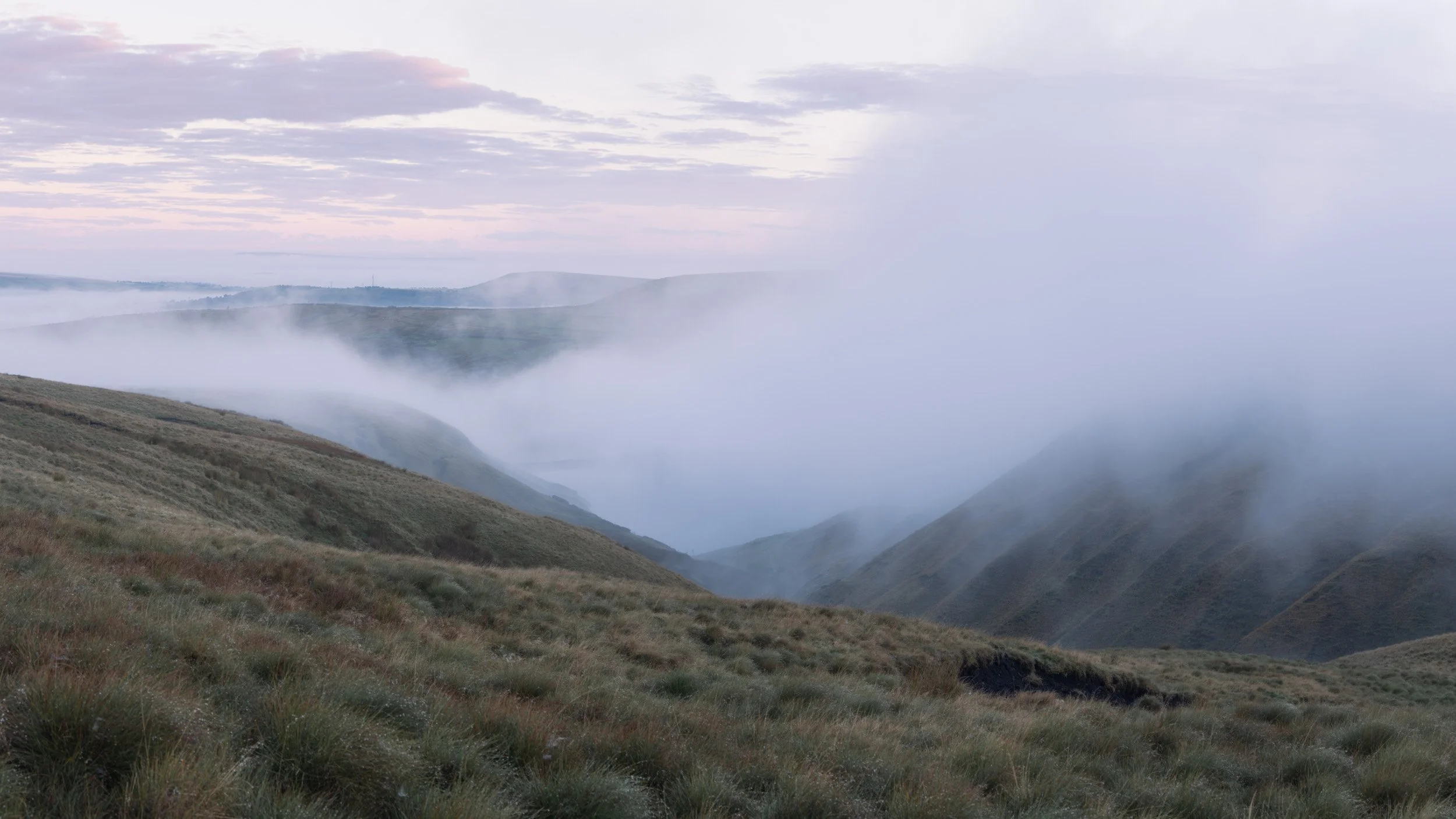 Wide panoramic view of a cloud inversion spilling over the hills at Scout Moor High Level Reservoir during early morning light, capturing the quiet solitude of neurodivergent photography.