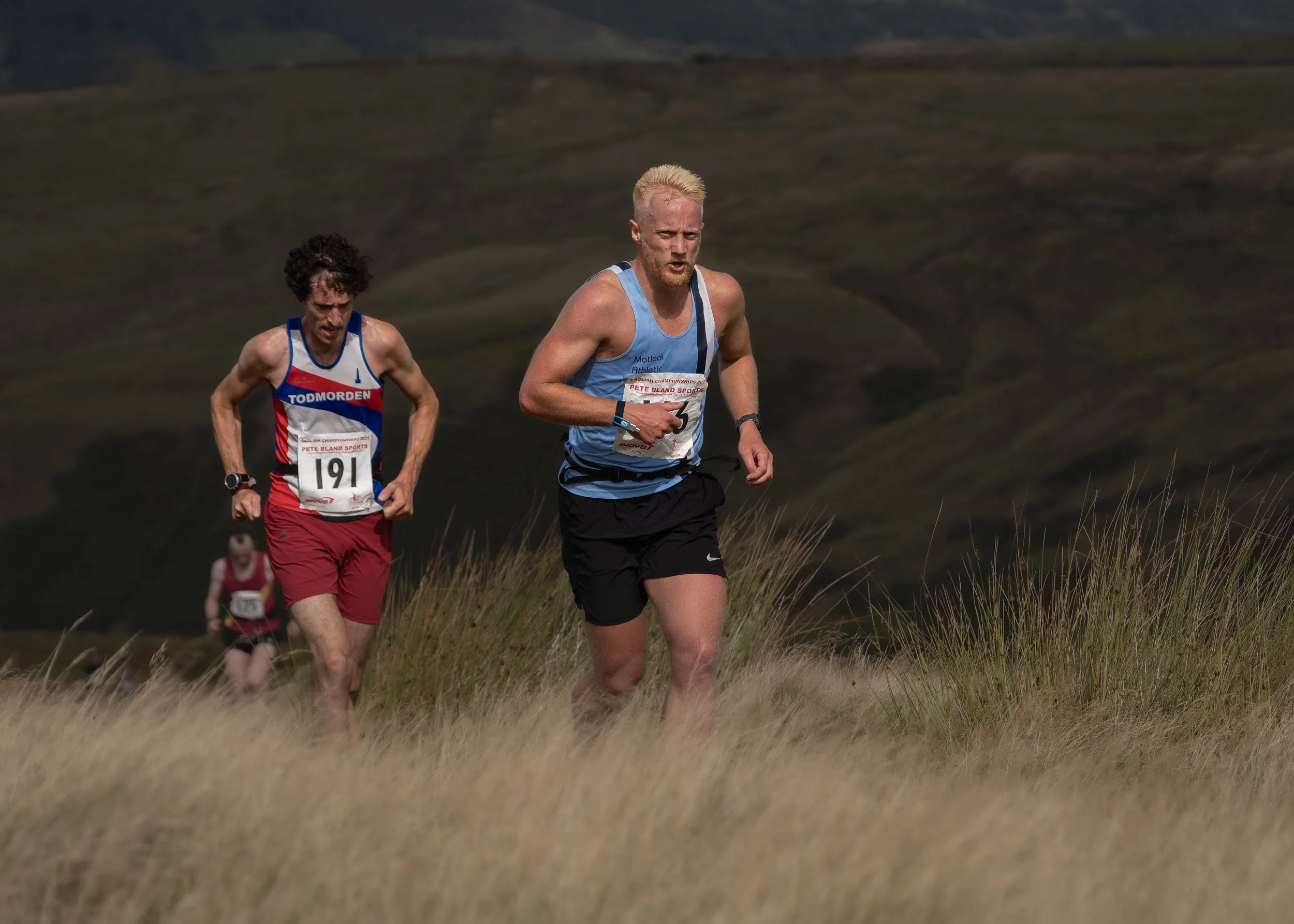 Todmorden Harriers runner (#191) chasing a rival in a light blue singlet up a grassy ridge on Scout Moor.
