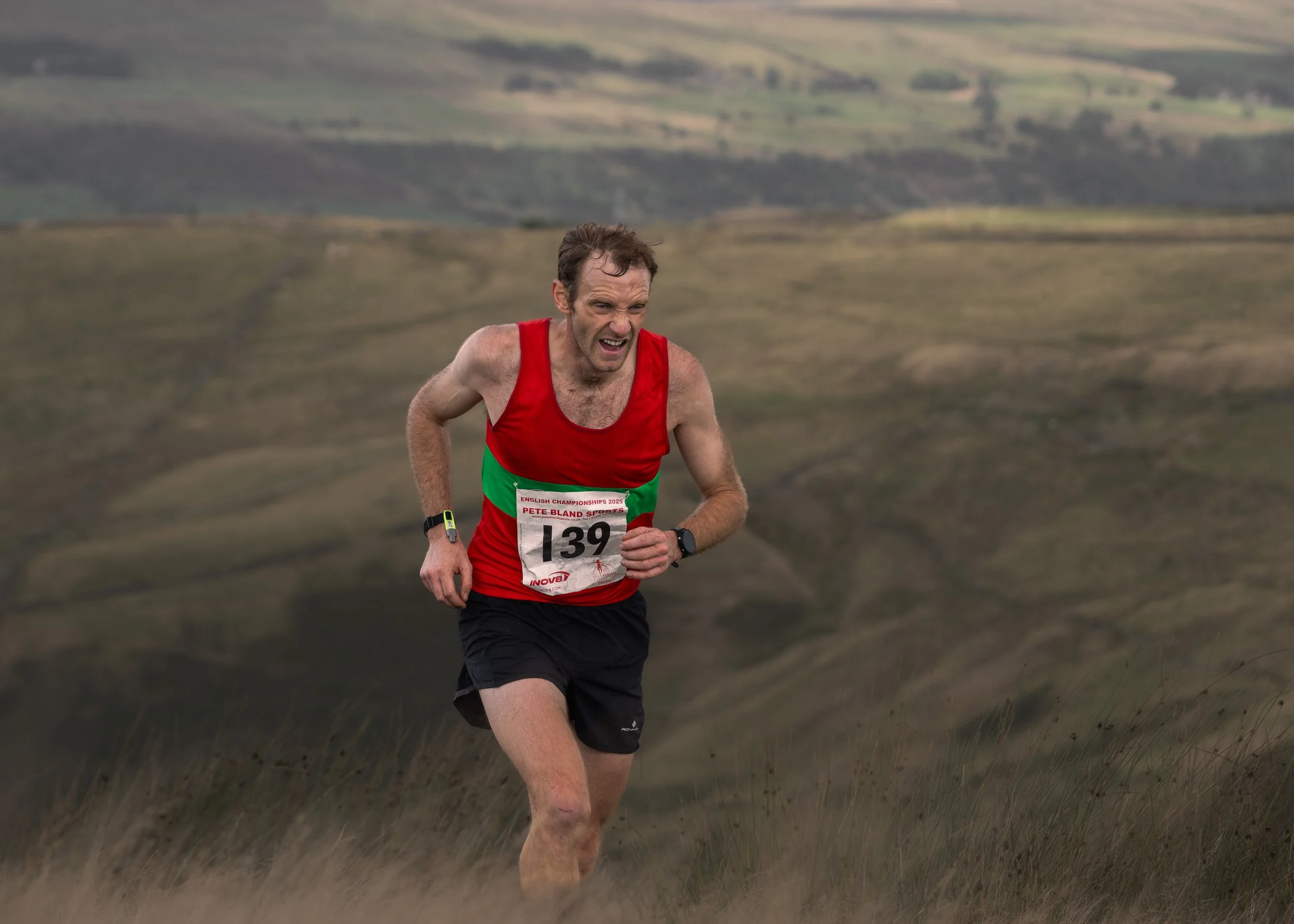 Fell runner wearing race number 139 in a red vest digging deep on a grassy incline during the Whittle Pike race on Scout Moor.