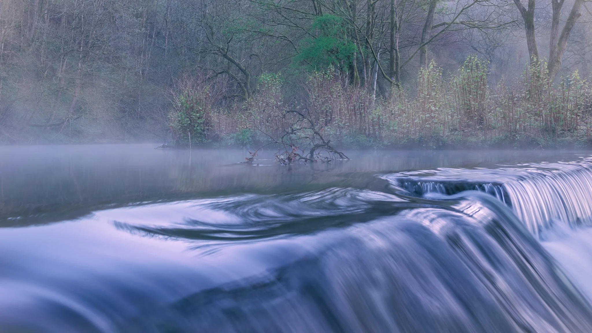 Weir on the river roch in full flow with mist drifting on the water by Ste Walton.
