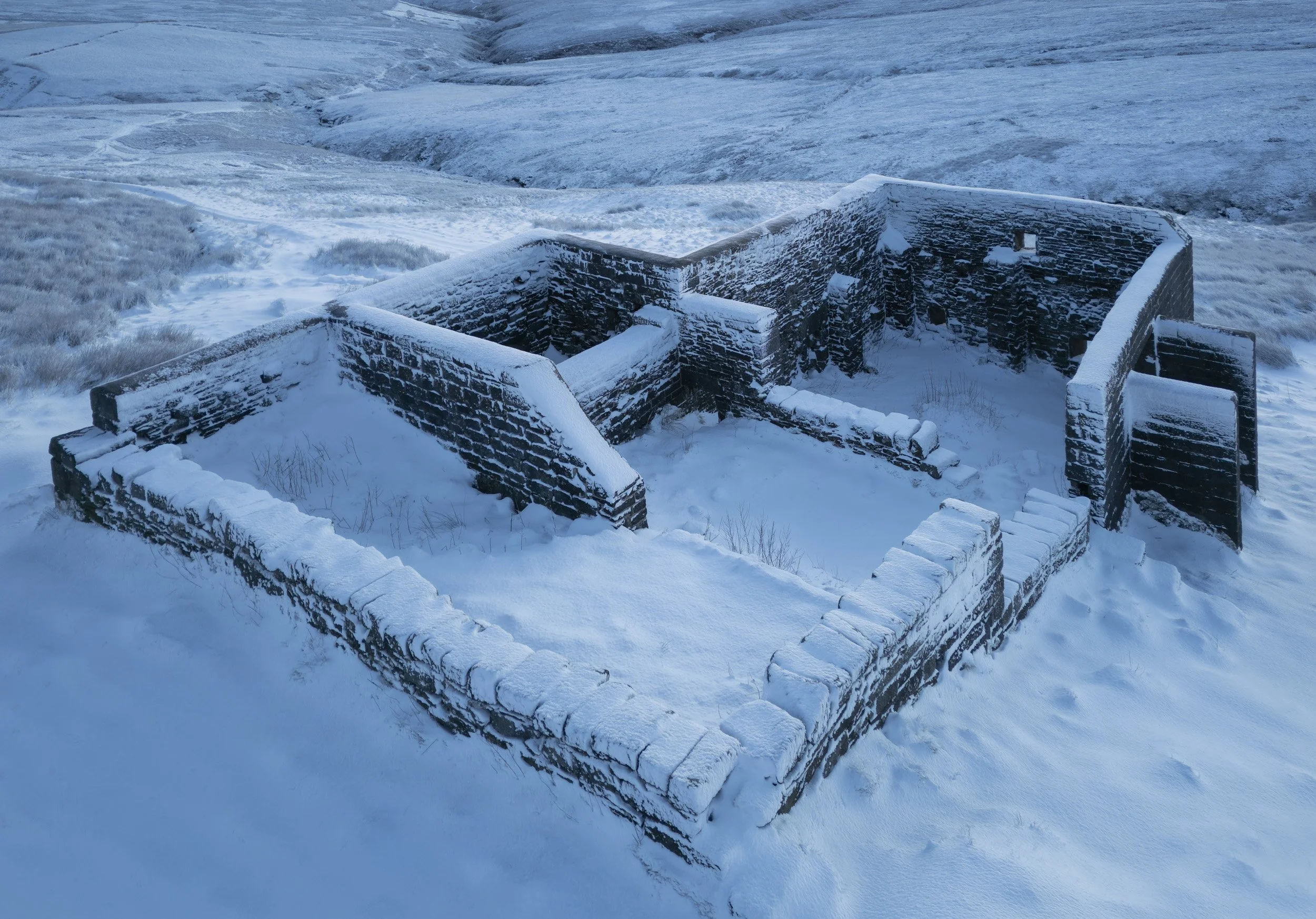 now-covered drystone ruins of Top Withens farmhouse, West Yorkshire, with the snow-laden moors in the background.