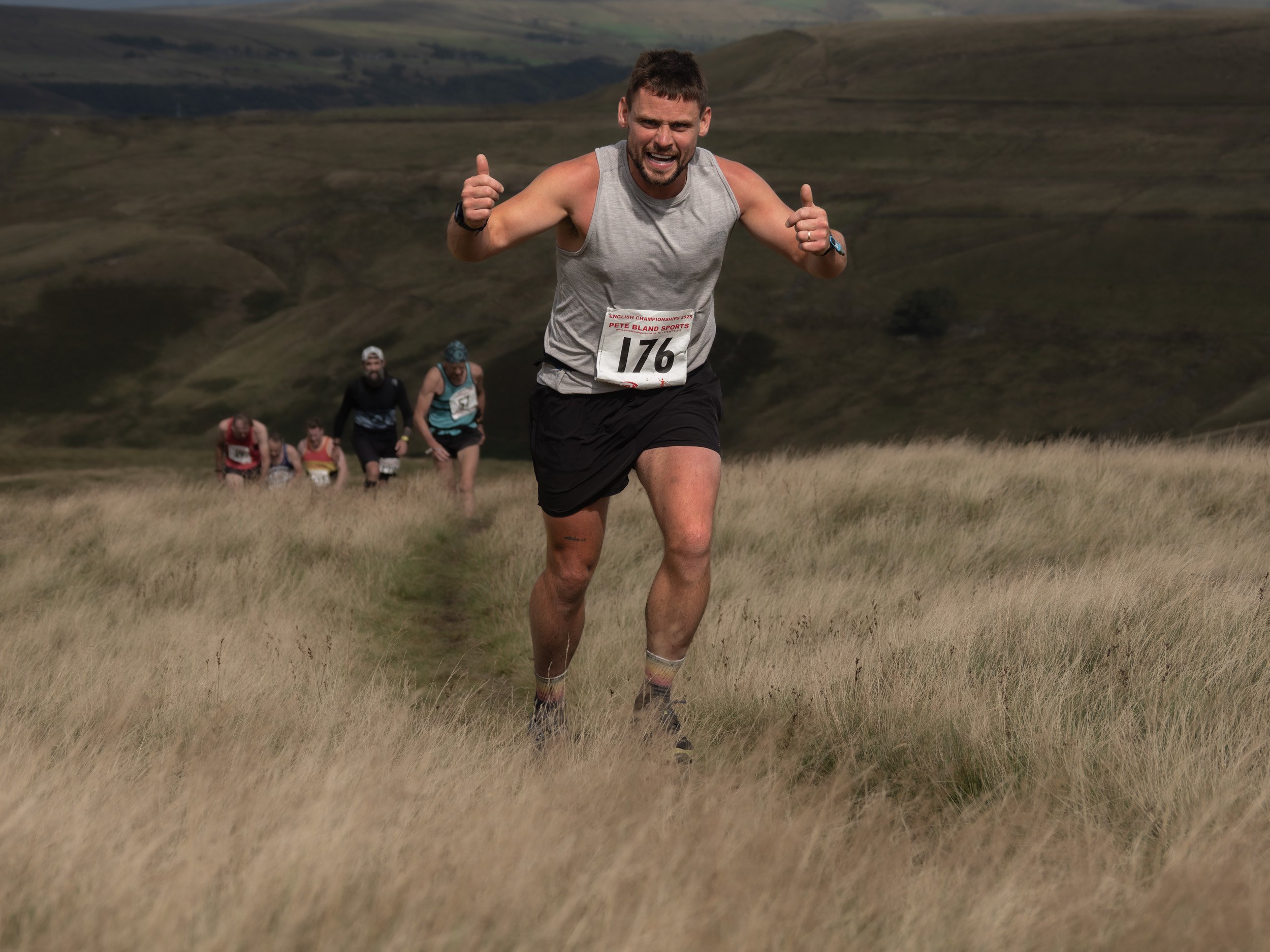 Smiling fell runner giving two thumbs up to the camera while sprinting ahead of competitors during the Whittle Pike race.