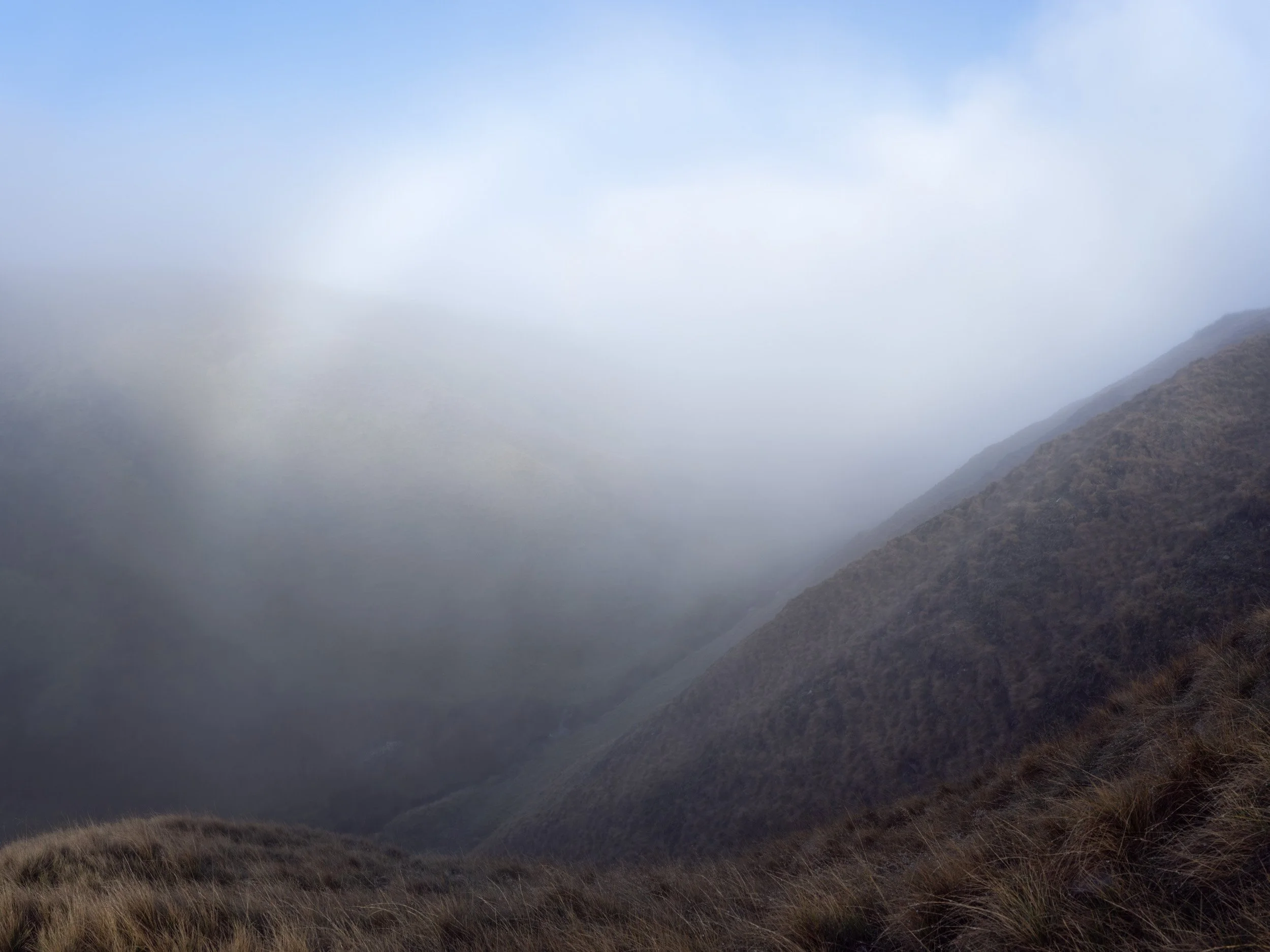 Thick white fog and soft shafts of light forming a fogbow filling the valley leading down into Scout Moor High Level Reservoir.