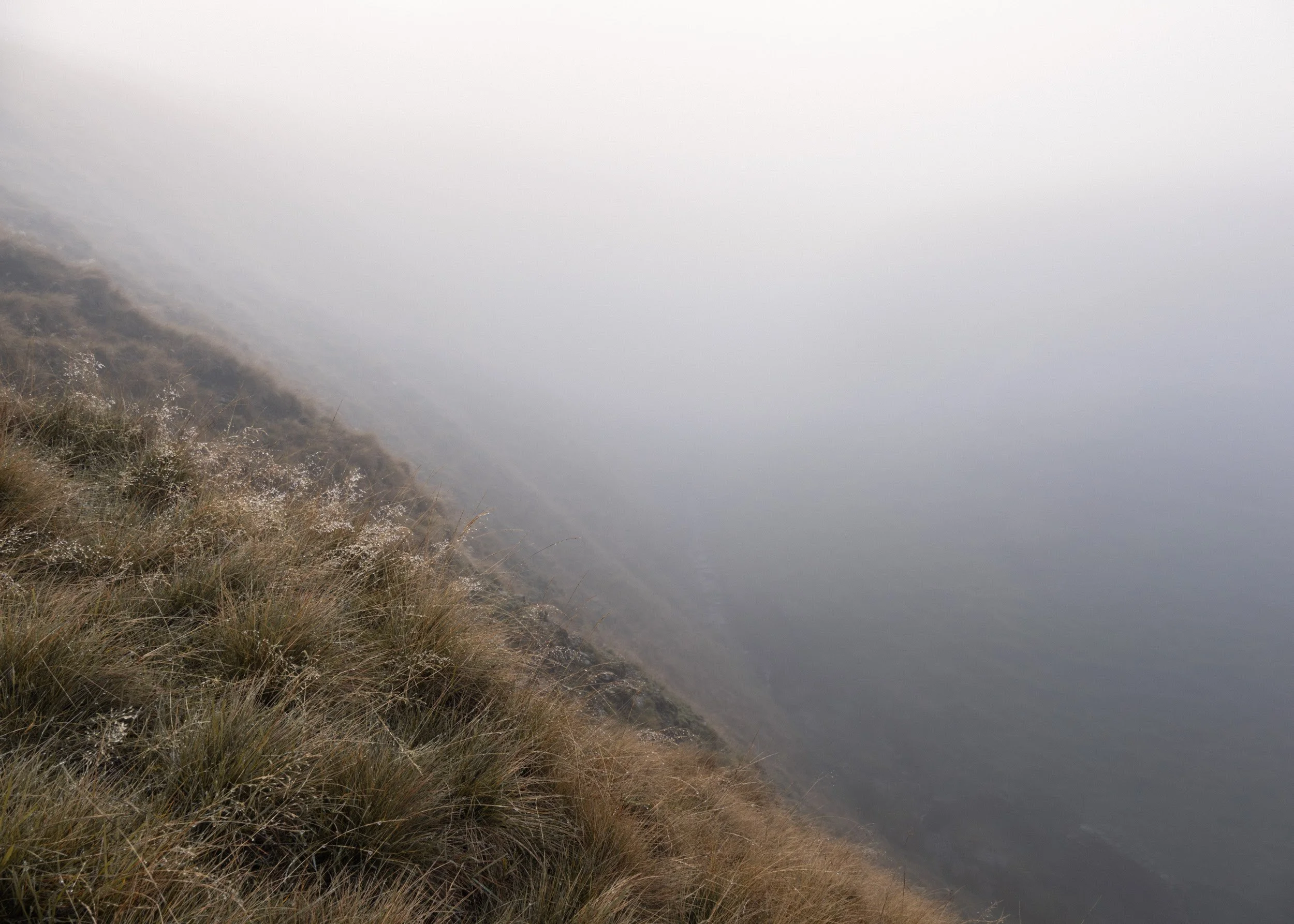 Minimalist landscape of a steep, grassy moorland slope disappearing into thick, heavy fog above Scout Moor Brook.