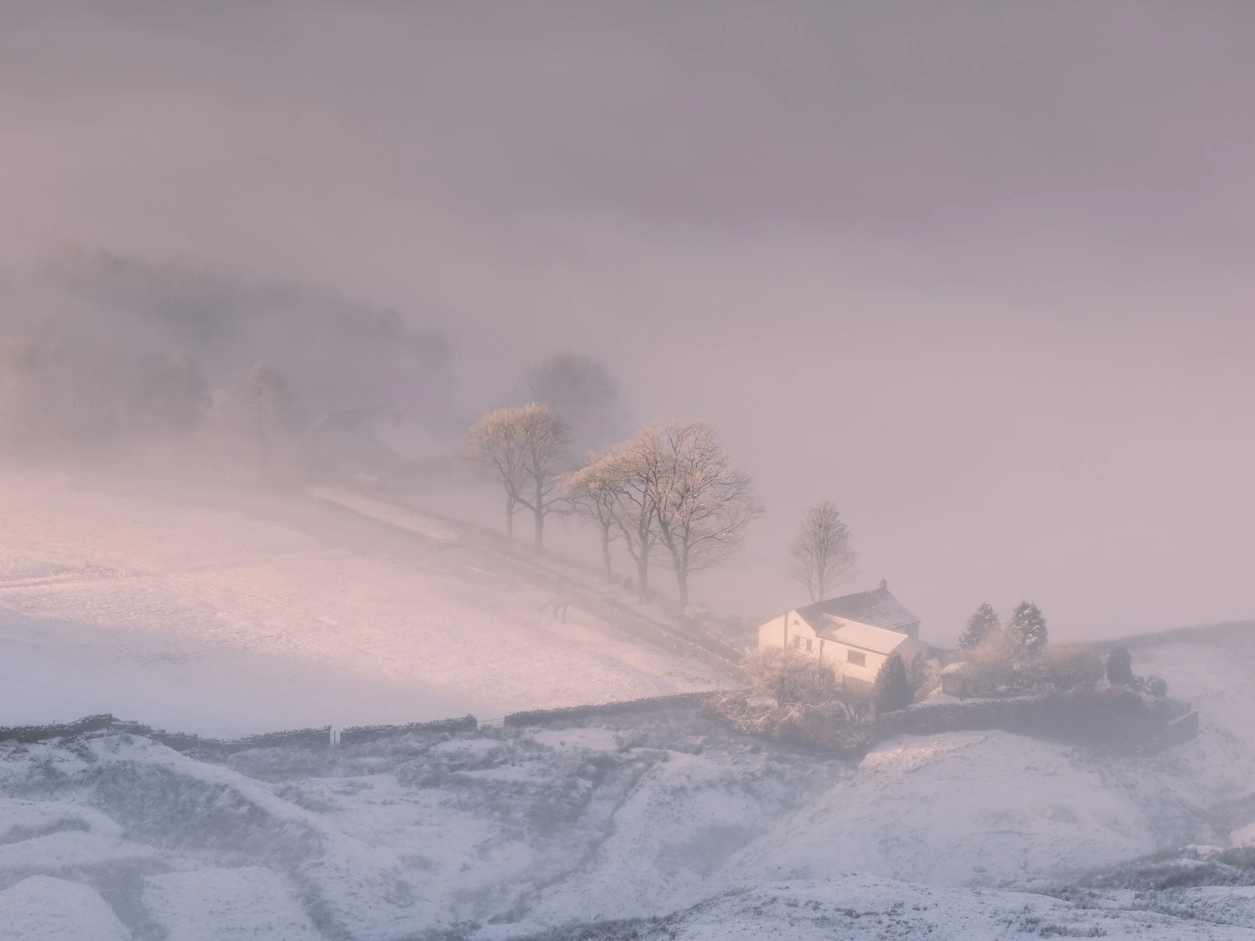 Newgate Farm in Newgate Valley, Rossendale, surrounded by snow and illuminated by a soft shaft of warm sunlight breaking through thick morning fog.