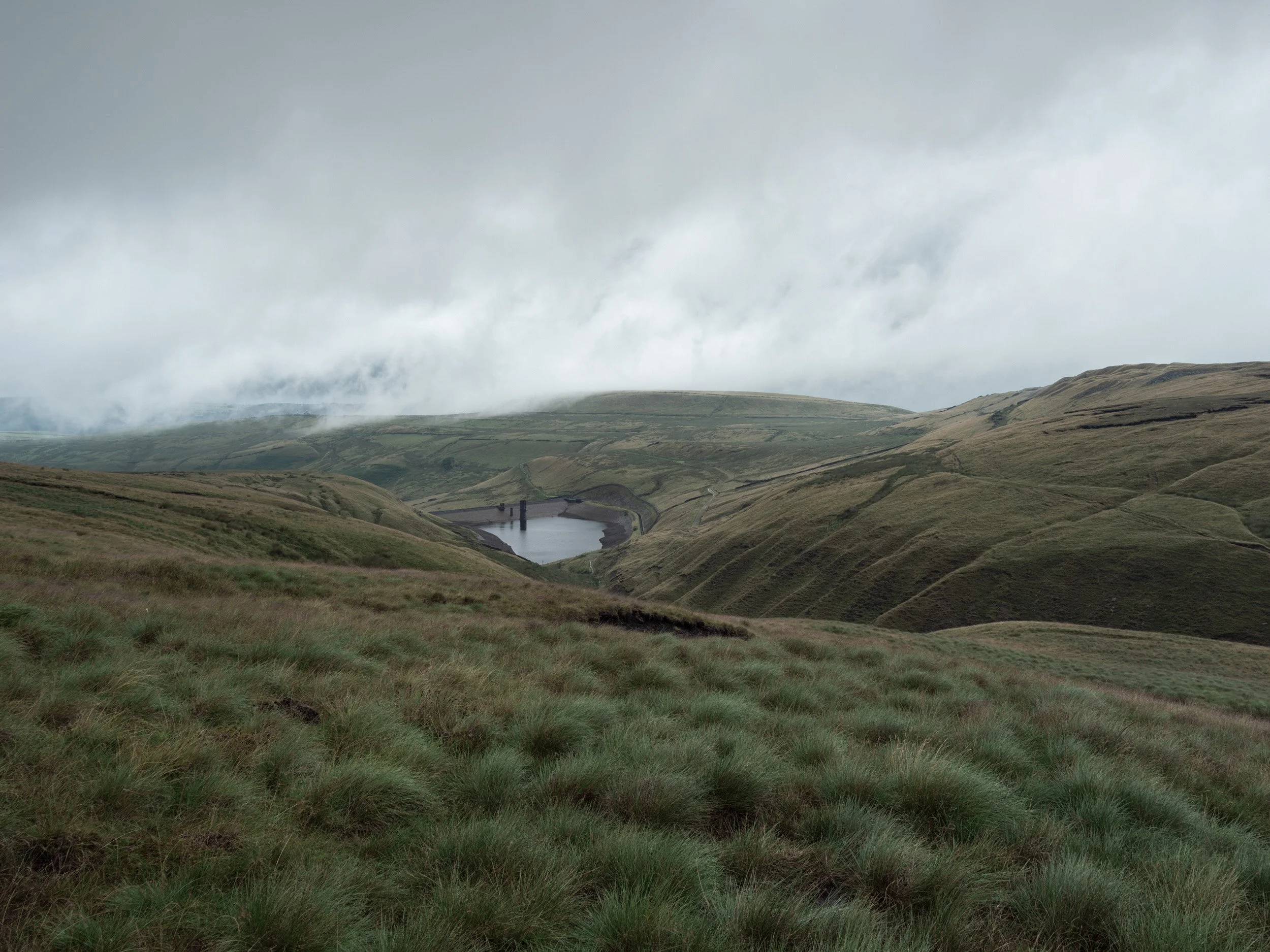 Low-hanging clouds and fog sweeping across the hills above Scout Moor High Level Reservoir.