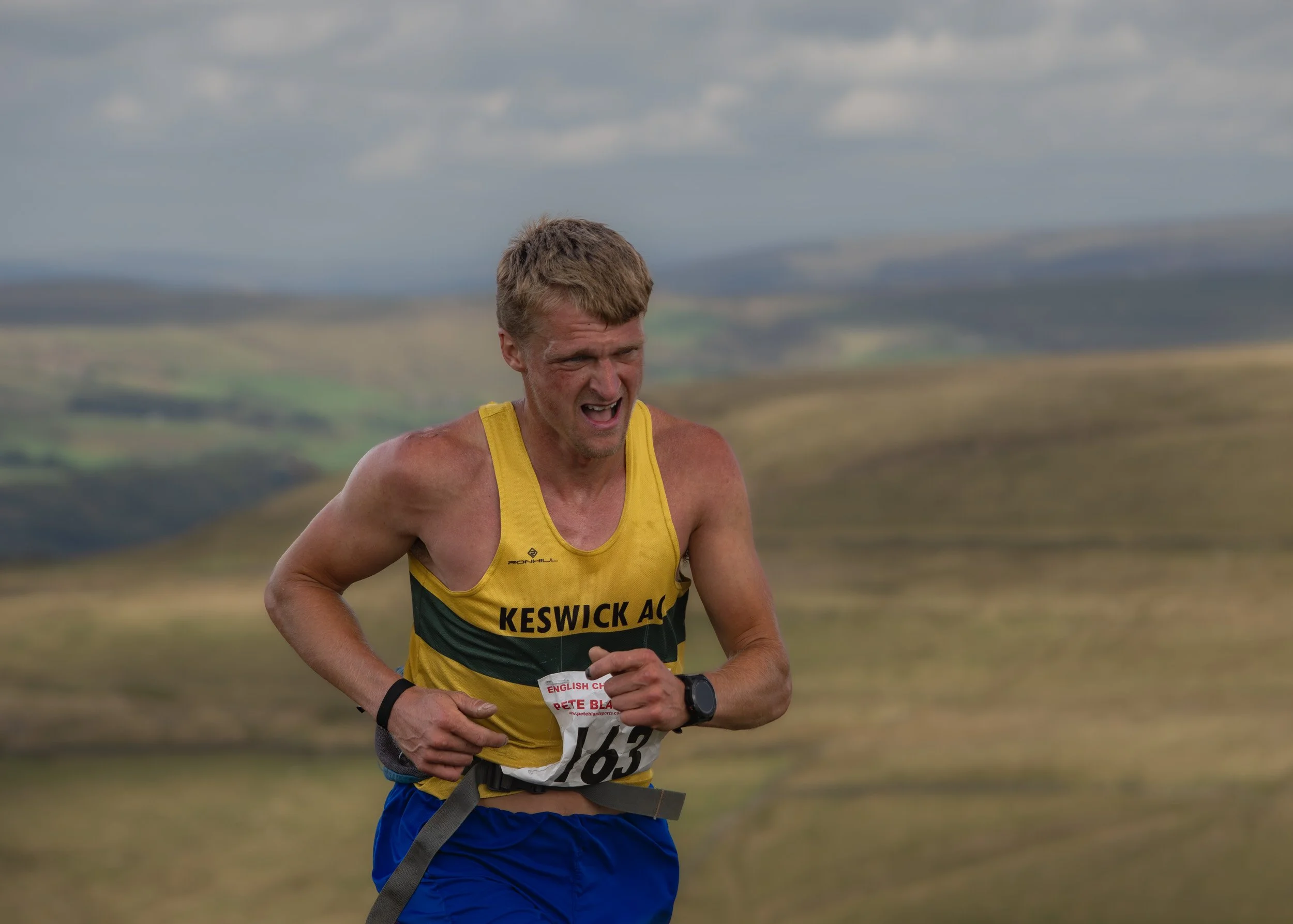 Mid-shot of a Keswick AC fell runner gritting his teeth in intense effort on the Whittle Pike Fell Race course near Scout Moor.