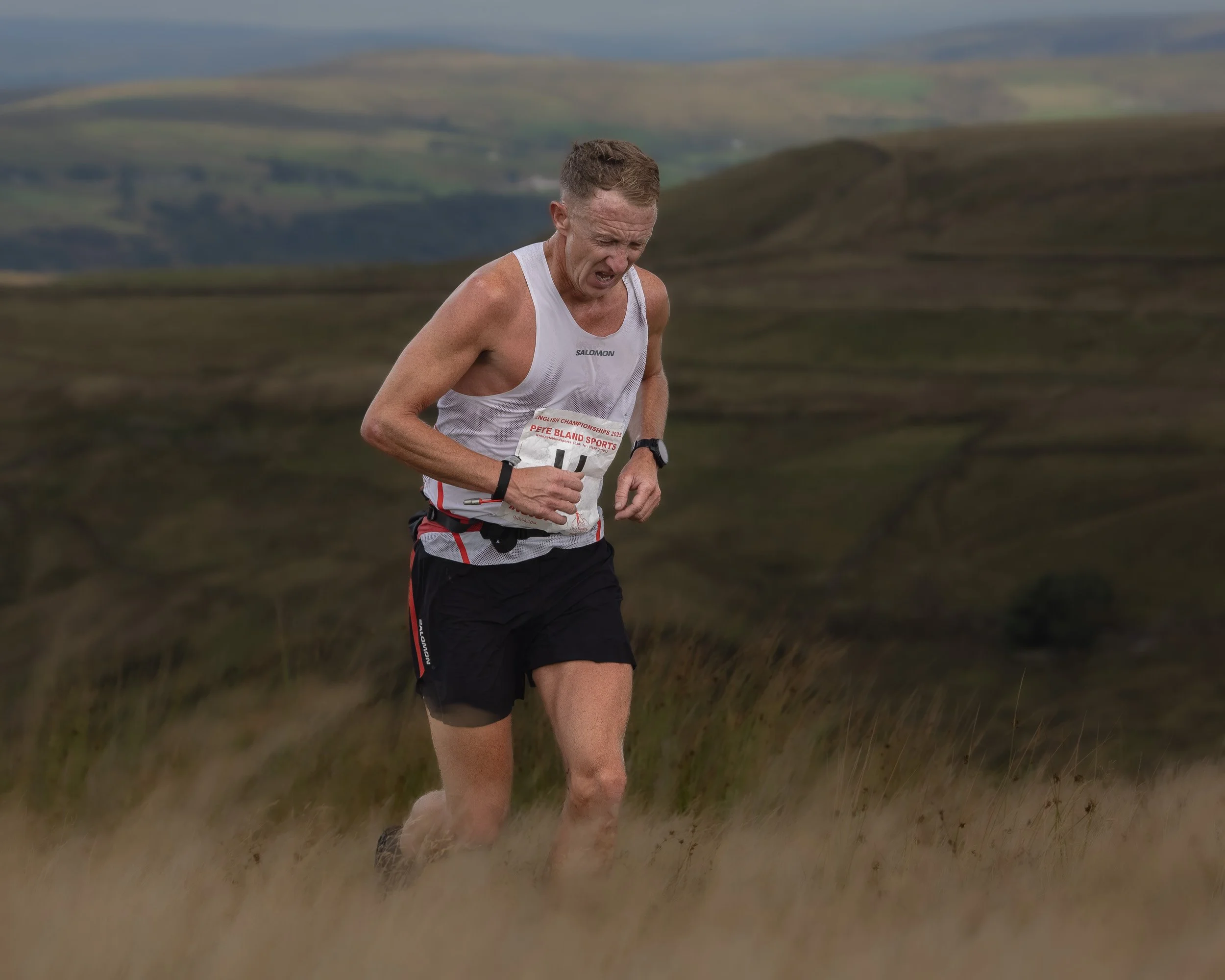 Focused fell runner in a white Salomon singlet powering up a moorland trail during the Whittle Pike Fell Race.