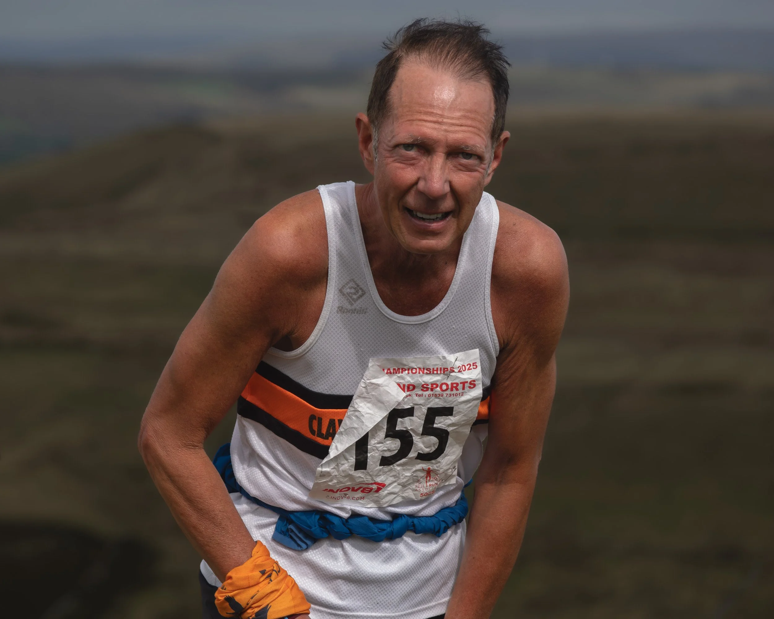 Fell runner in a white and orange Clayton-le-Moors Harriers vest (#155) leaning forward with a pained expression on Scout Moor.