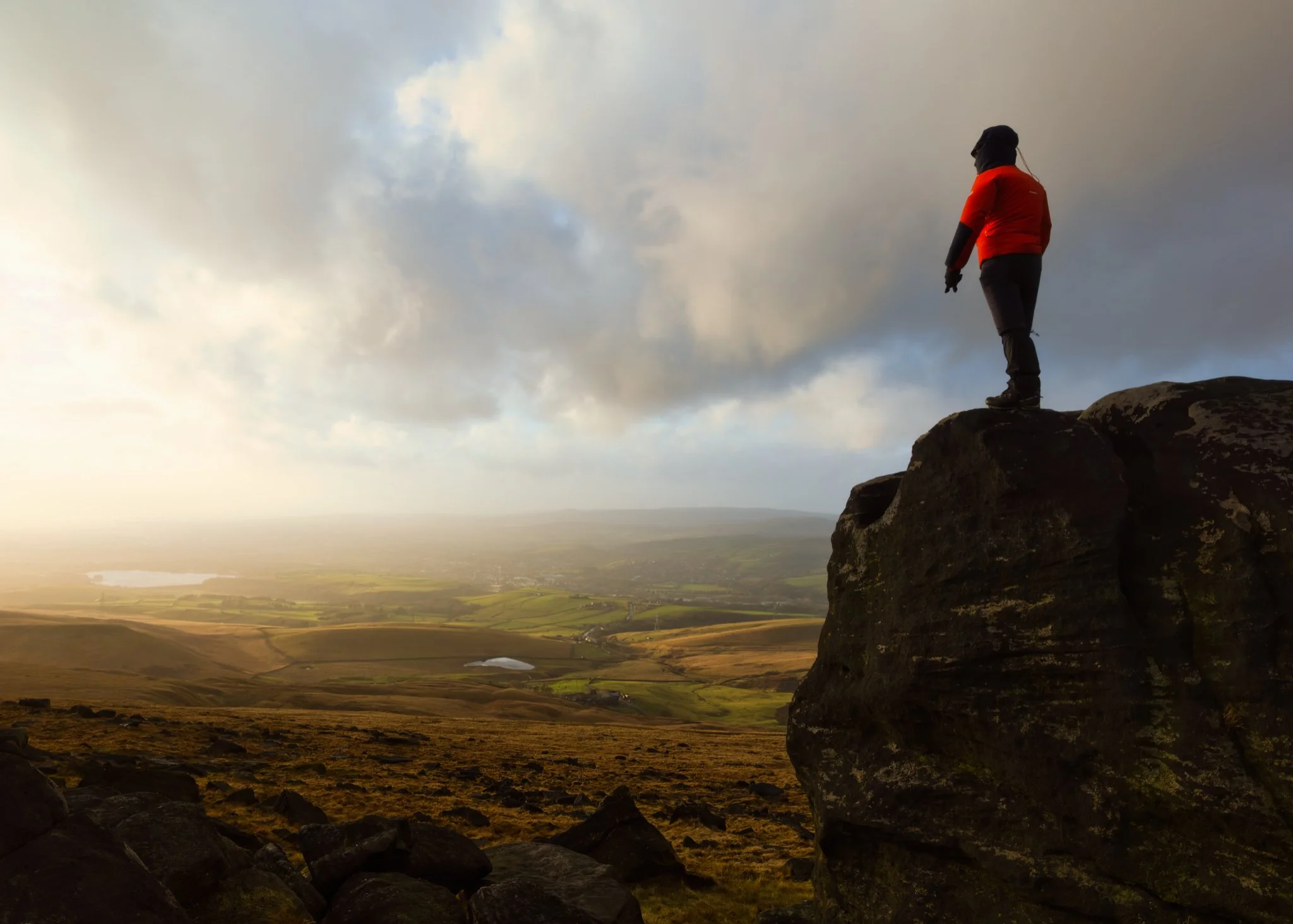Photographer in a red jacket standing atop Robin Hood's Bed rock formation on Blackstone Edge at sunset after a storm.